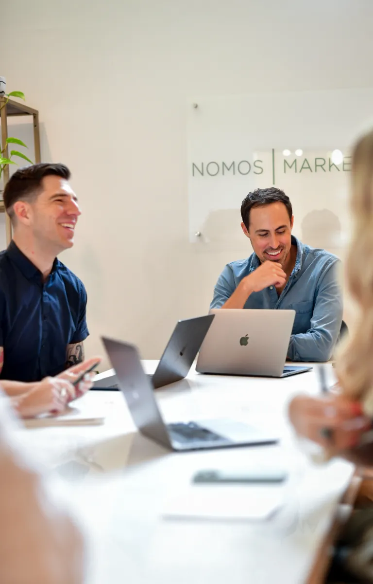 Two men at a conference table, laughing with their marketing team.