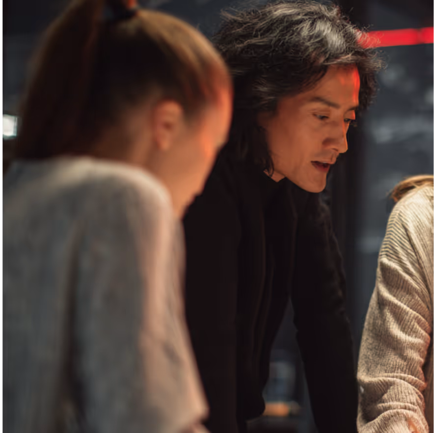 Three people engaged in a discussion, focusing on a middle person with long hair speaking attentively.