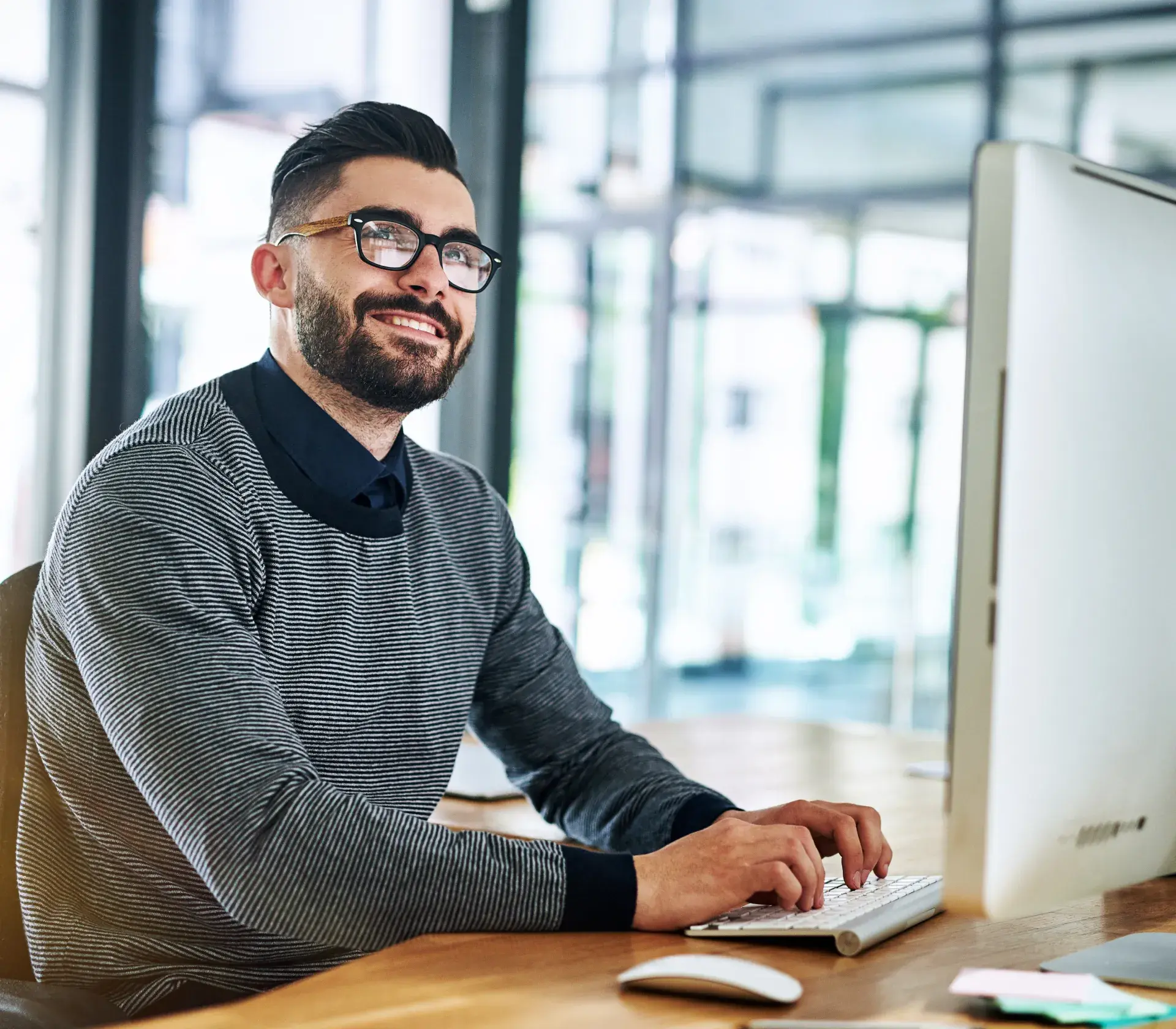 Woman wearing glasses and a light gray hijab working on a laptop and desktop computer displaying code.