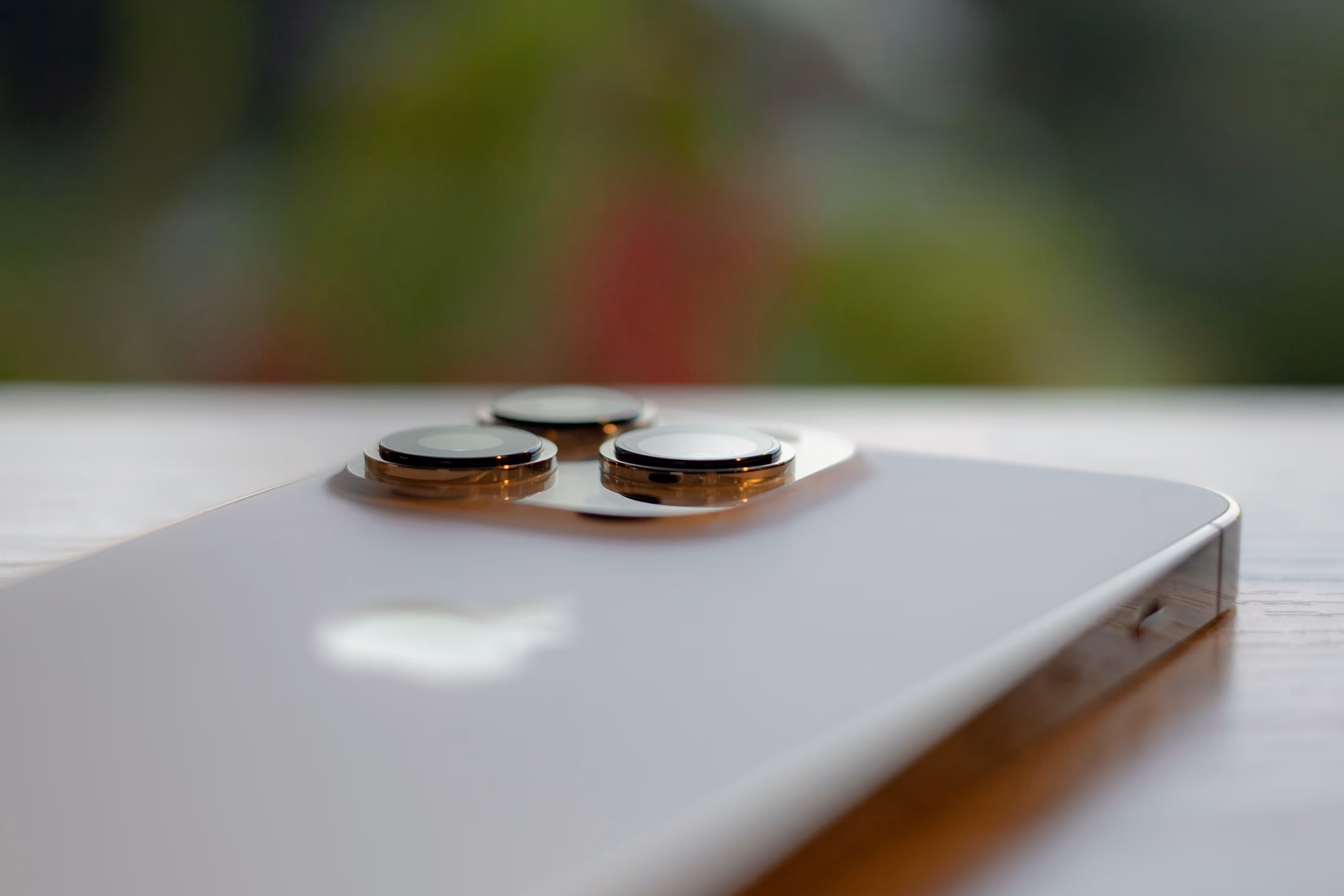 Close-up of the triple camera lenses on the back of an iPhone resting on a wooden surface.