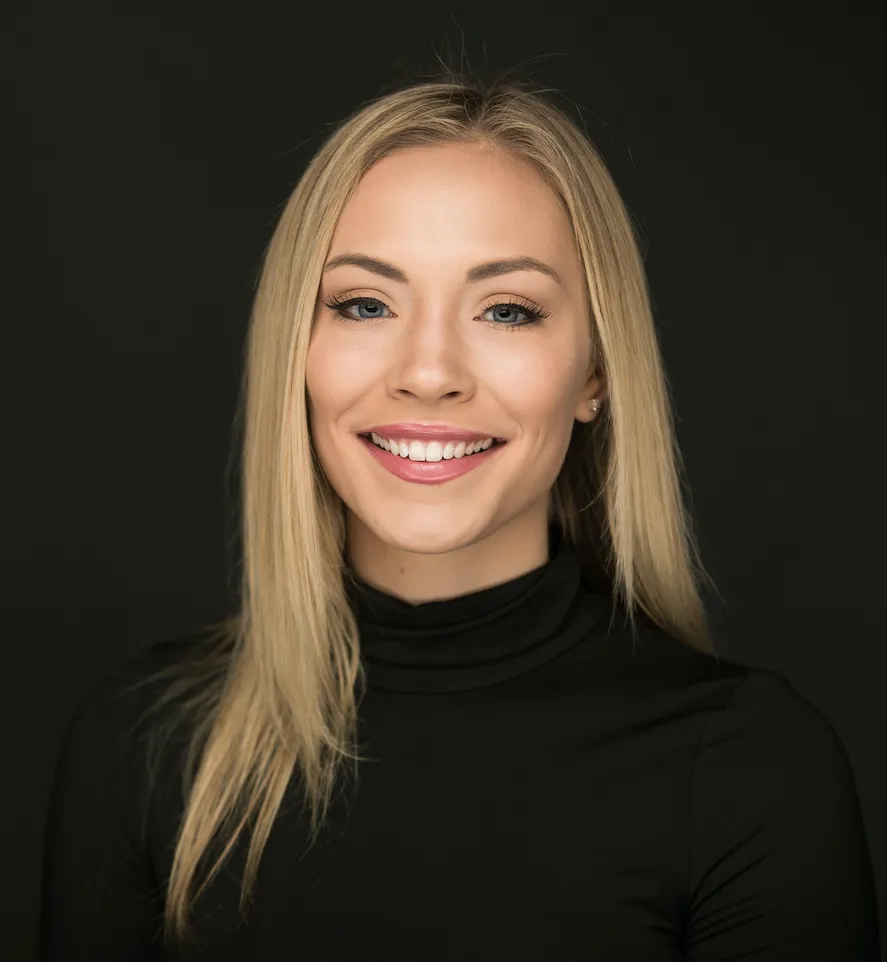 Smiling blonde woman with straight hair wearing a black turtleneck against a dark background at Legacy Dental Pasadena after getting her Invisalign.