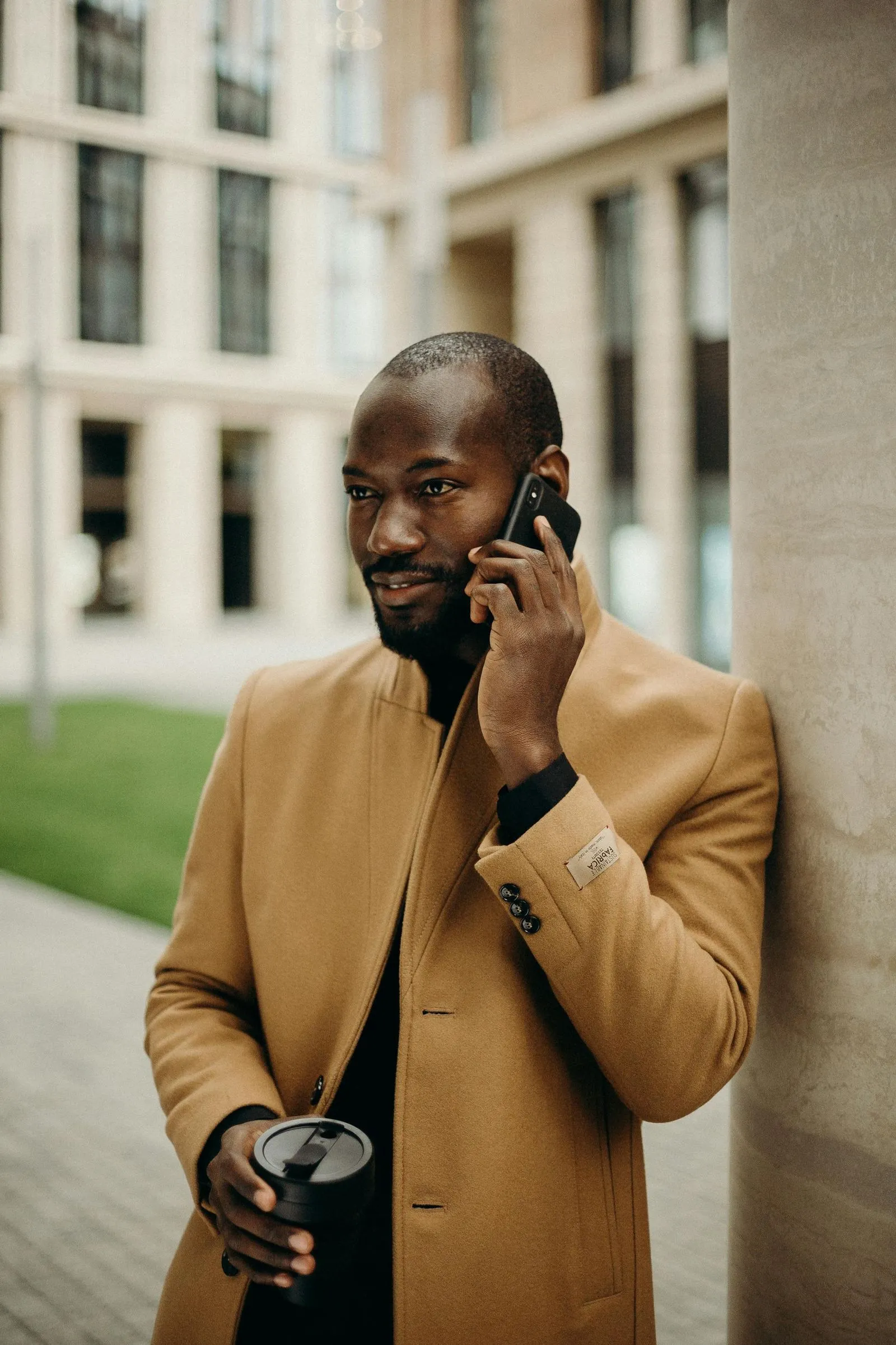 Man in a beige coat talking on the phone while holding a coffee cup