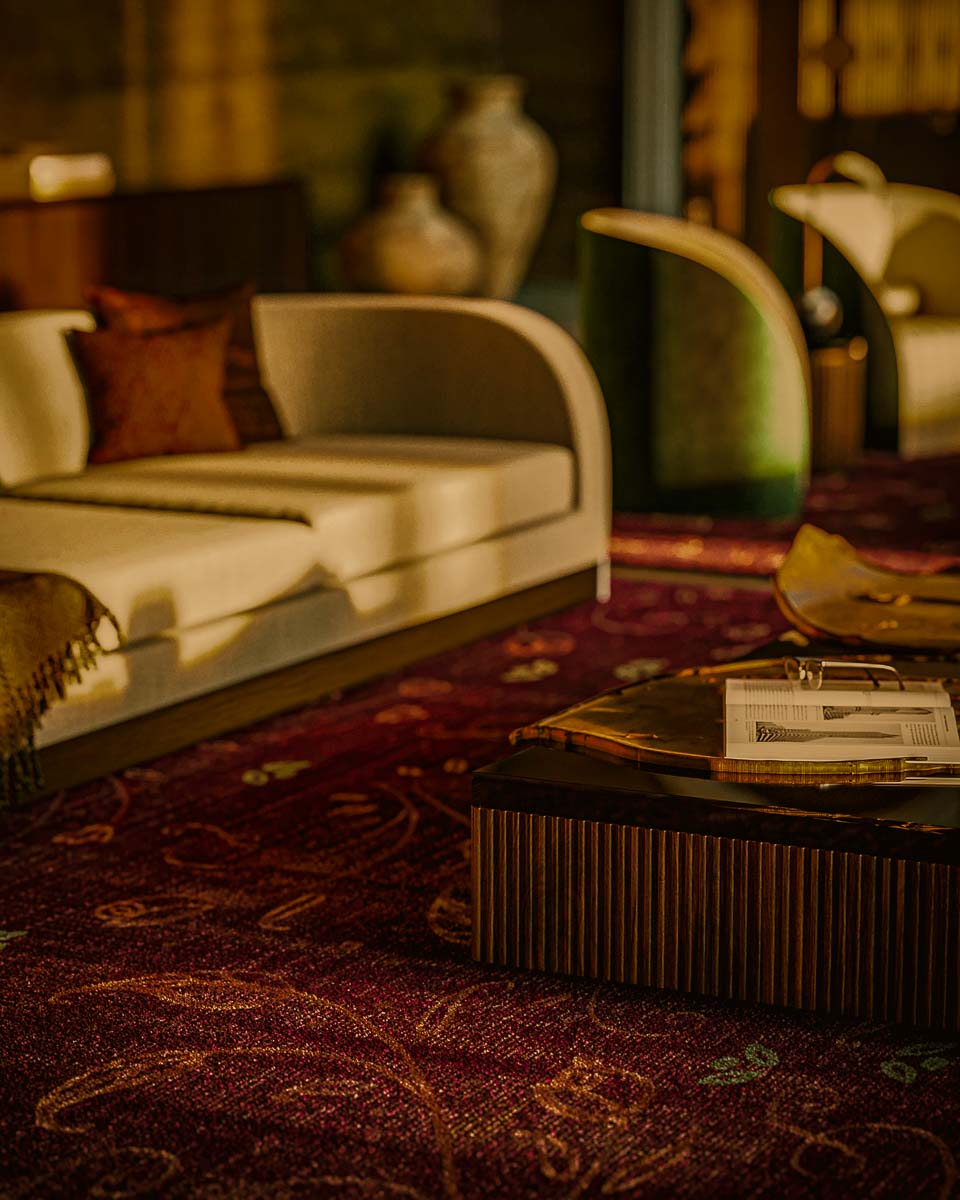 Cozy living room with beige sofa, patterned red carpet, wooden coffee table with an open book and eyeglasses, and decorative vases in the background.