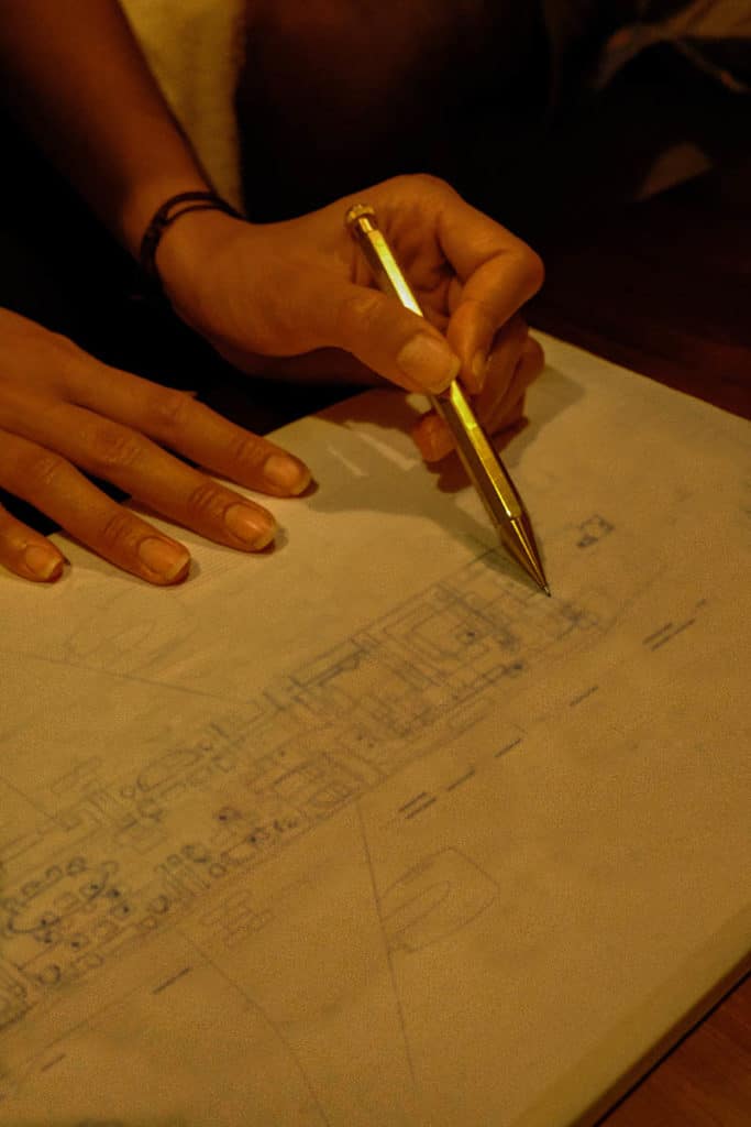 Close-up of hands sketching a detailed floor plan on paper with a gold pen.