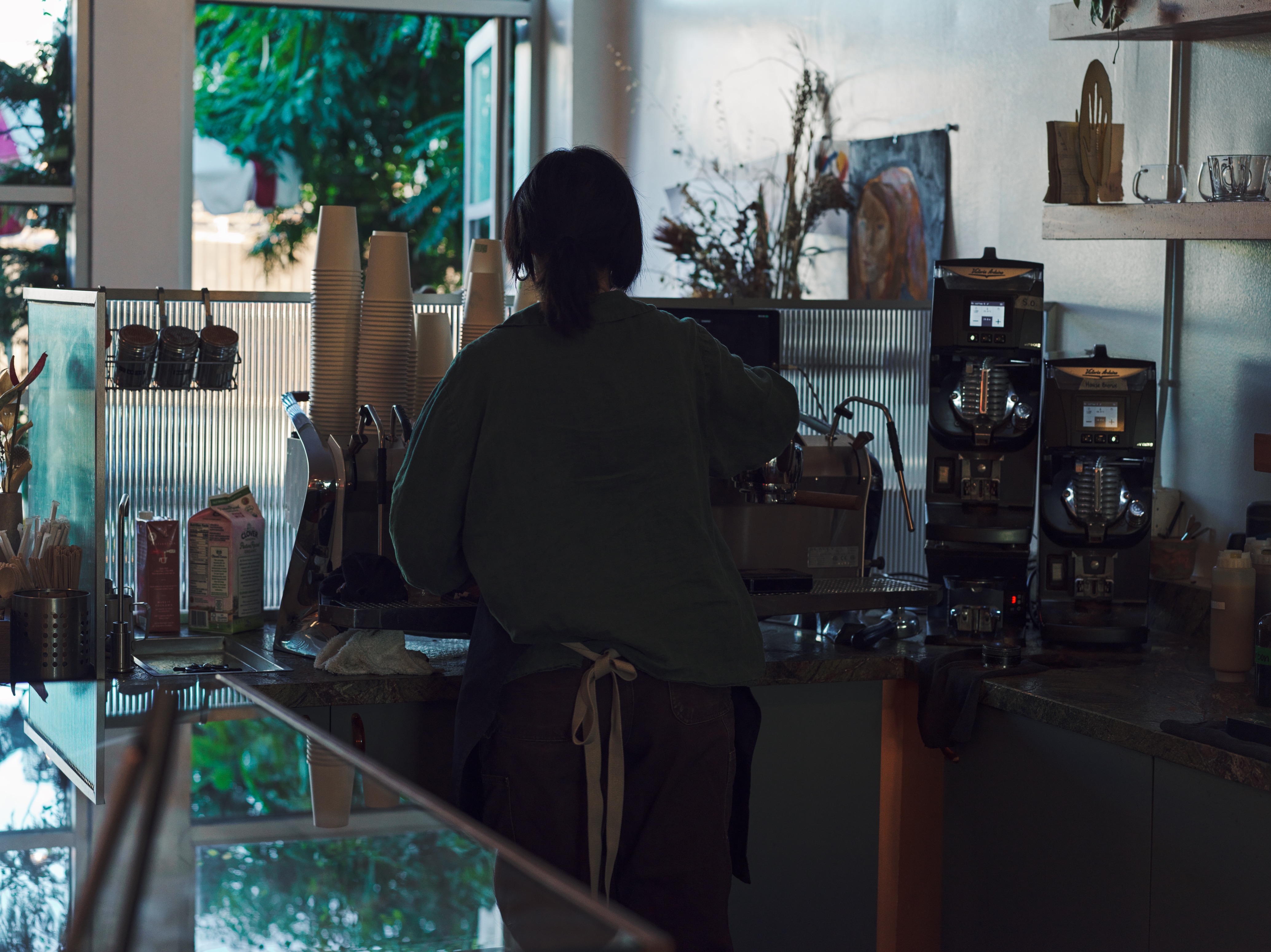 A barista working the espresso bar with bags of Jurassic Magic beans on the shelf behind