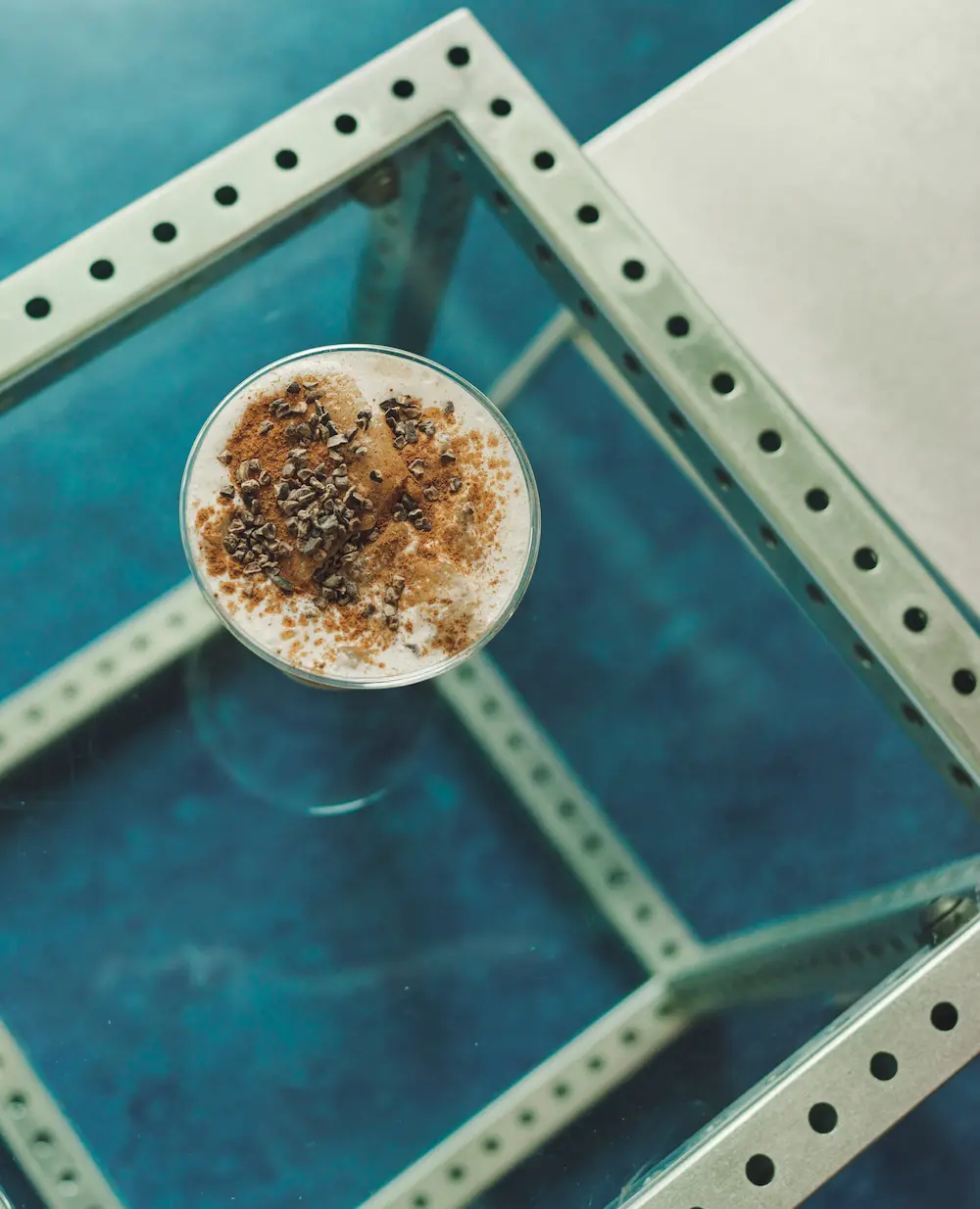 Iced drink topped with cinnamon and cacao nibs on a glass table