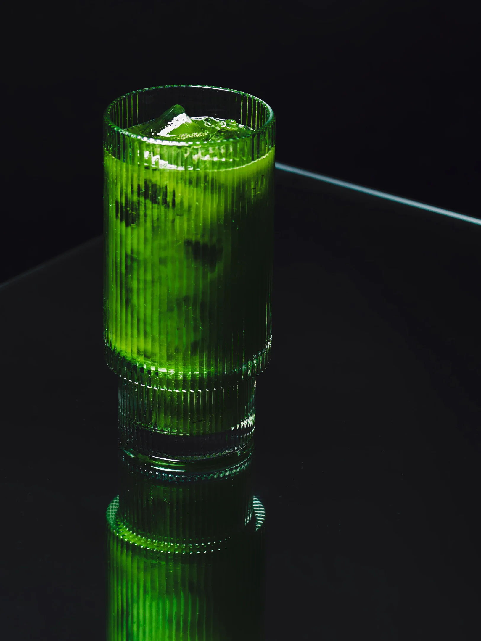 Bright green iced matcha drink with ice on a dark glass table