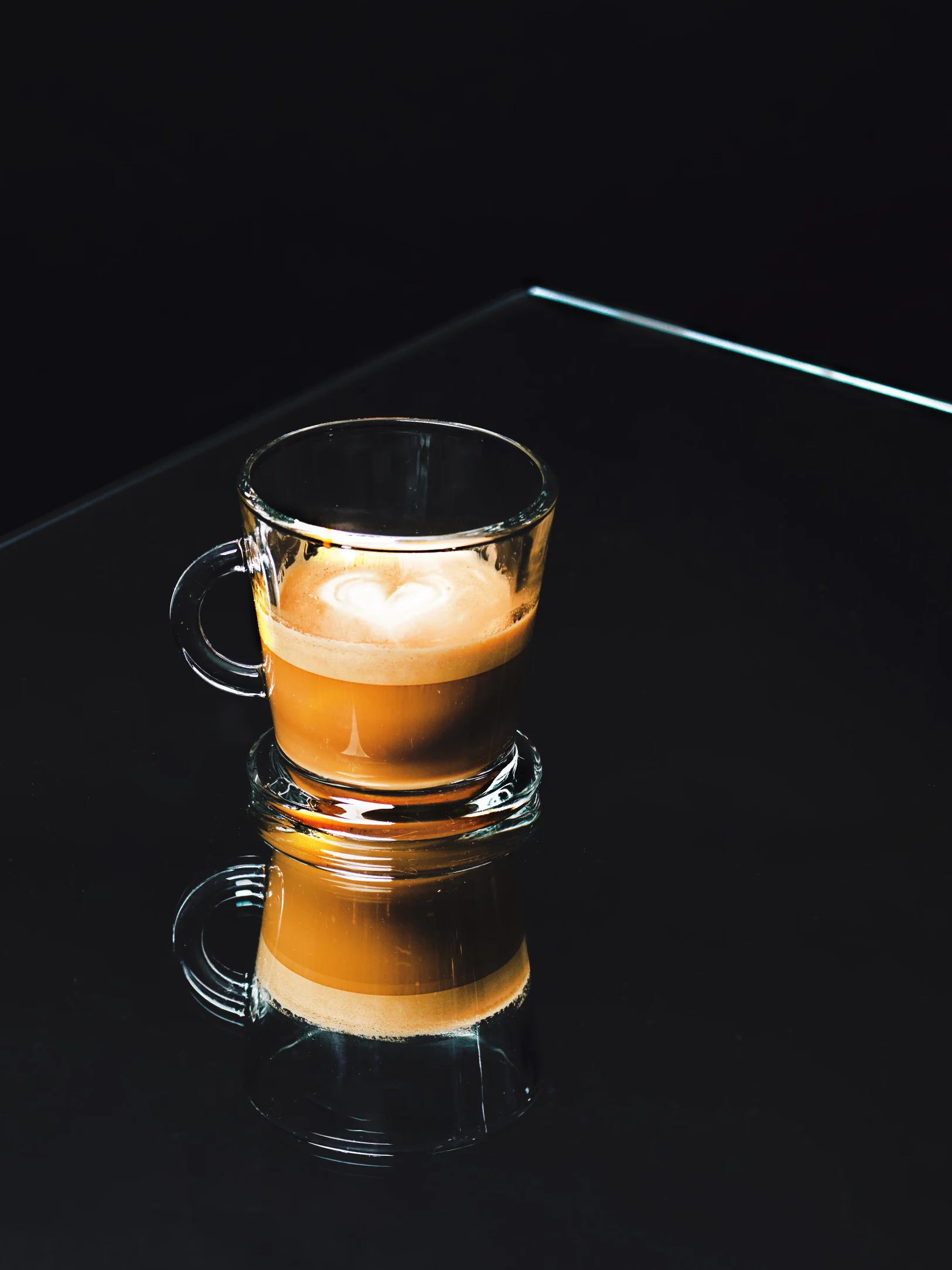 Cortado with heart latte art in a glass cup on a dark table