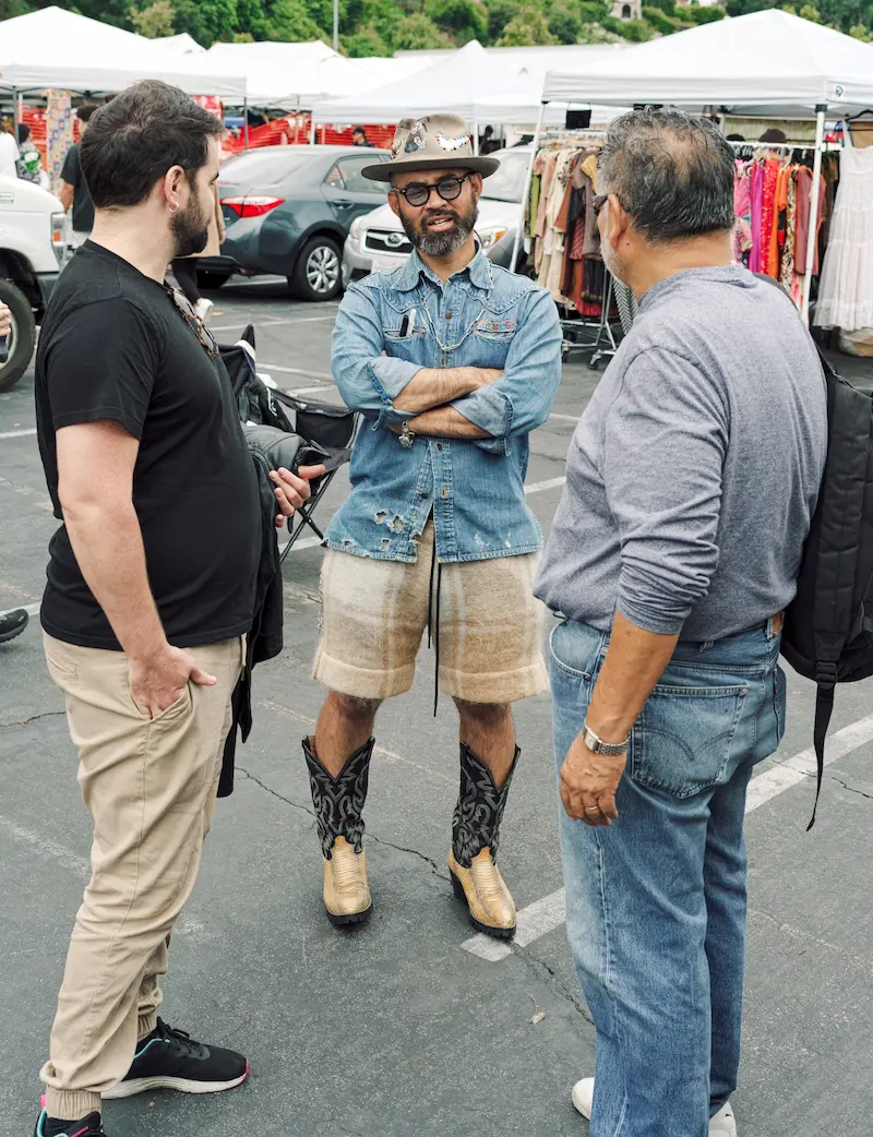 Two men chatting with a vendor at an outdoor flea market