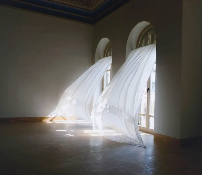 Sheer white curtains billowing through arched windows in a sunlit room