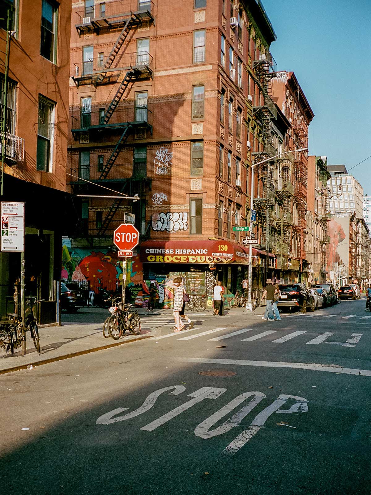 City street corner with a stop sign, bodega awning and pedestrians