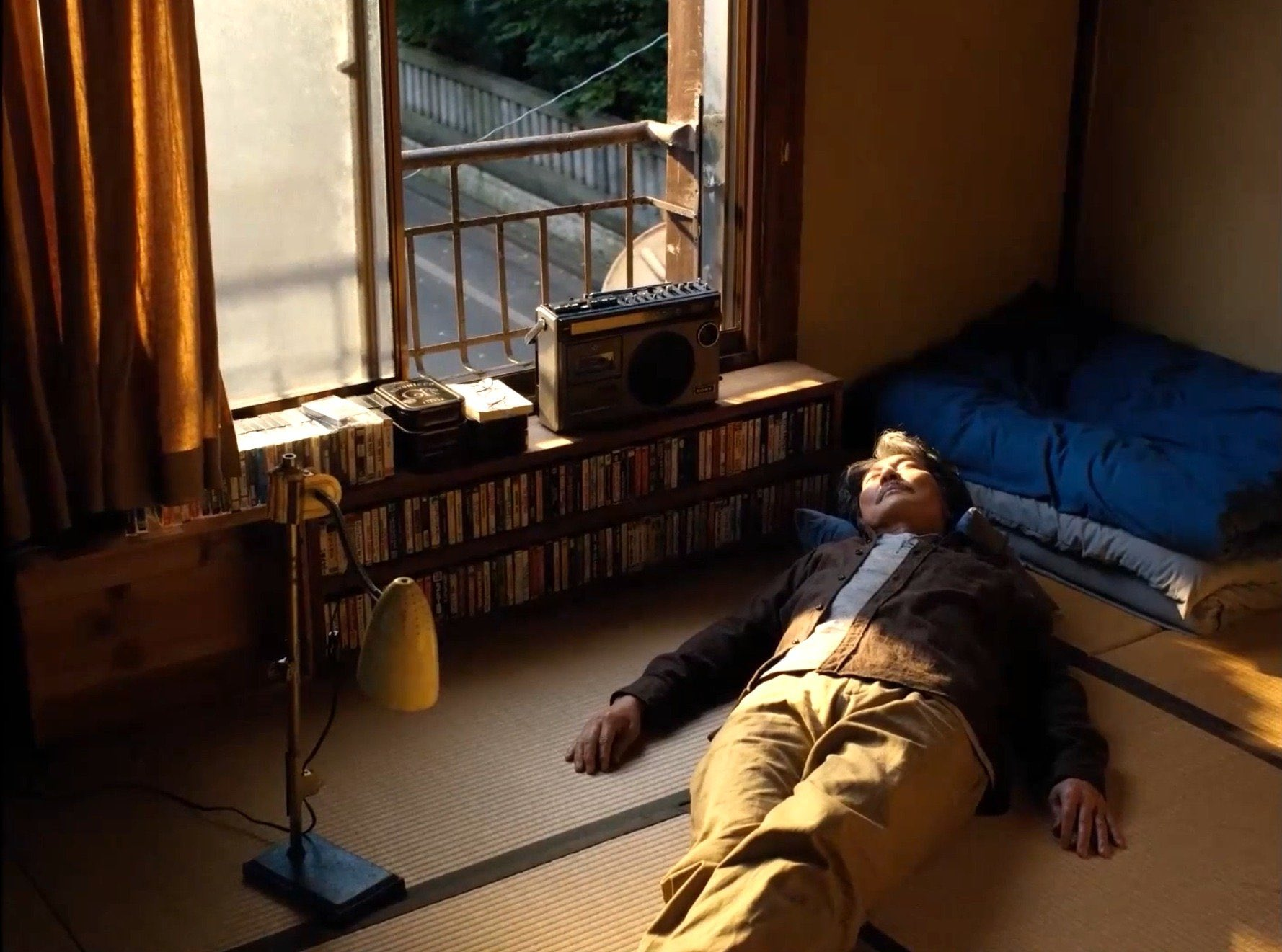 Person lying on a tatami floor beside a vintage boombox and record shelf