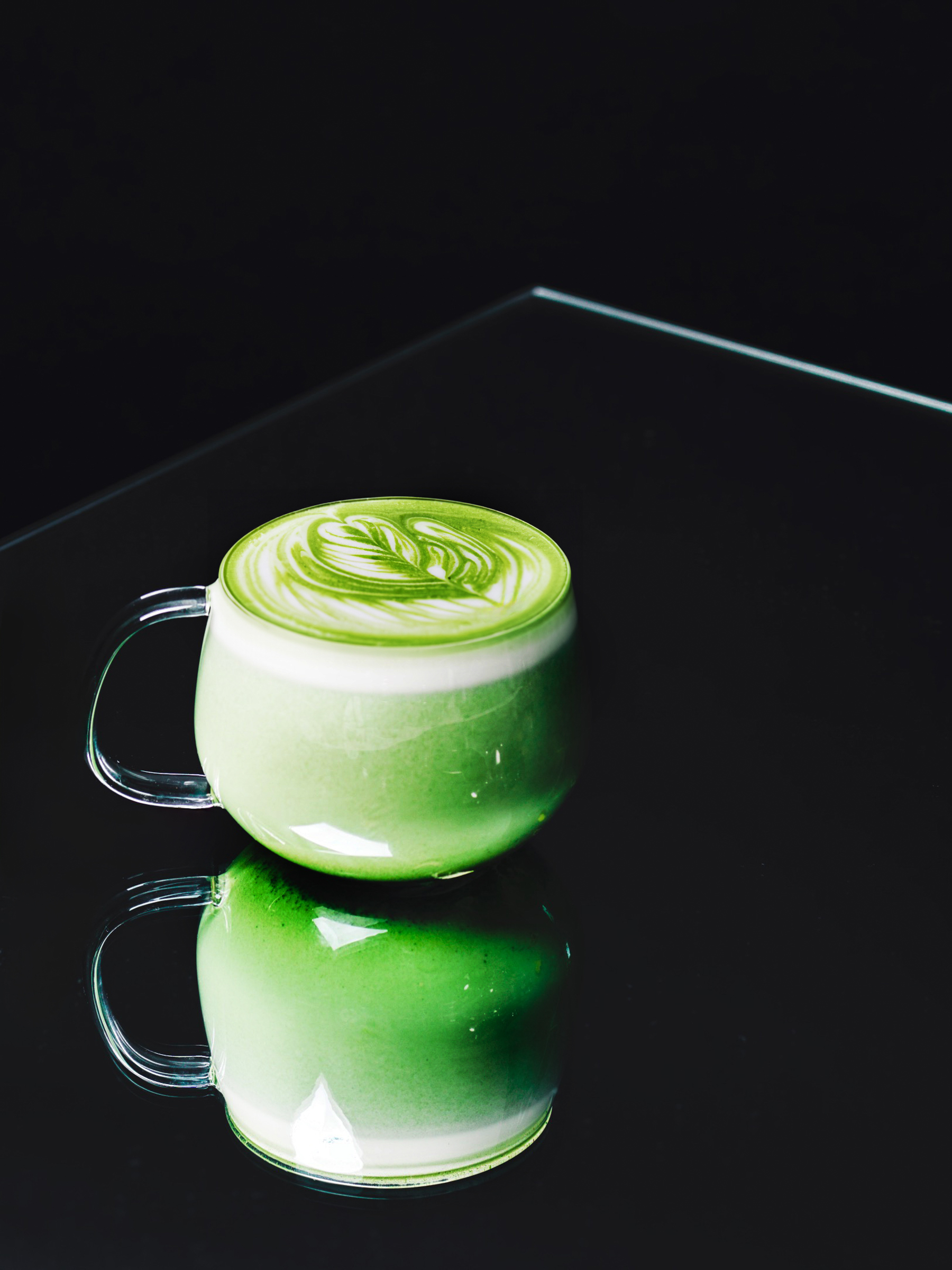 Matcha latte with leaf-pattern latte art in a glass mug on a dark table