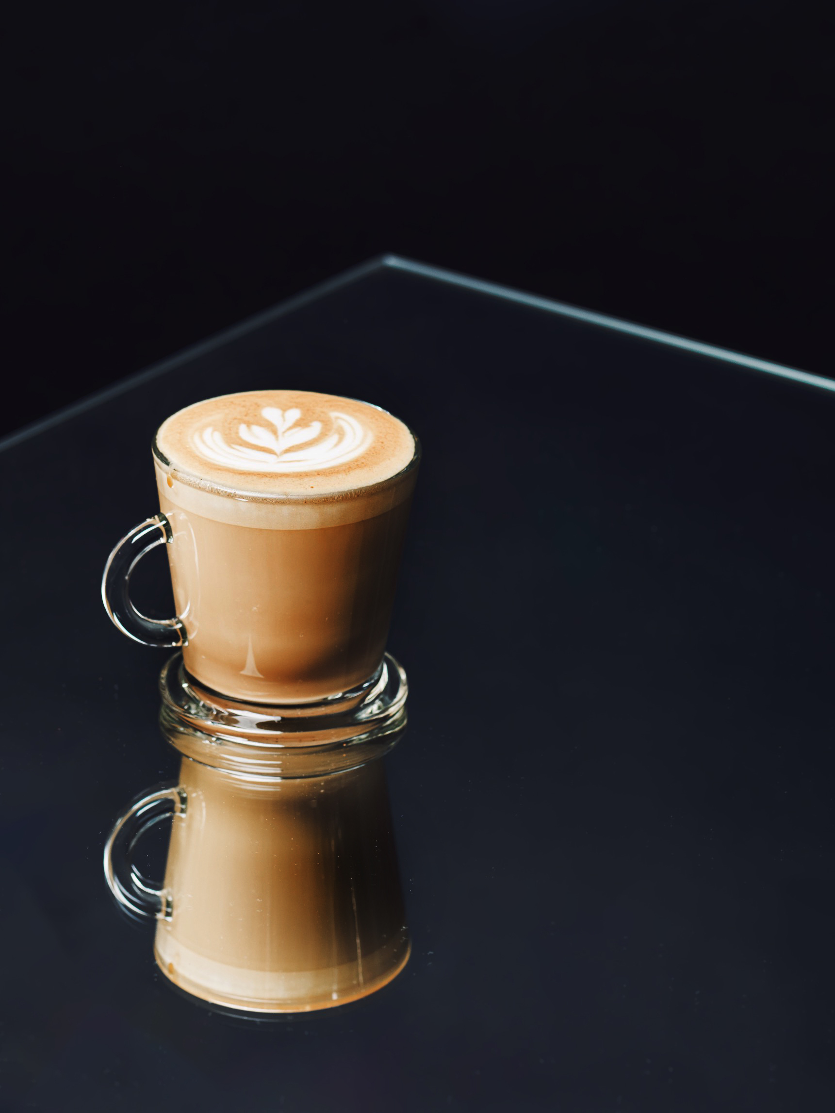 Flat white with heart latte art in a glass cup on a dark reflective table