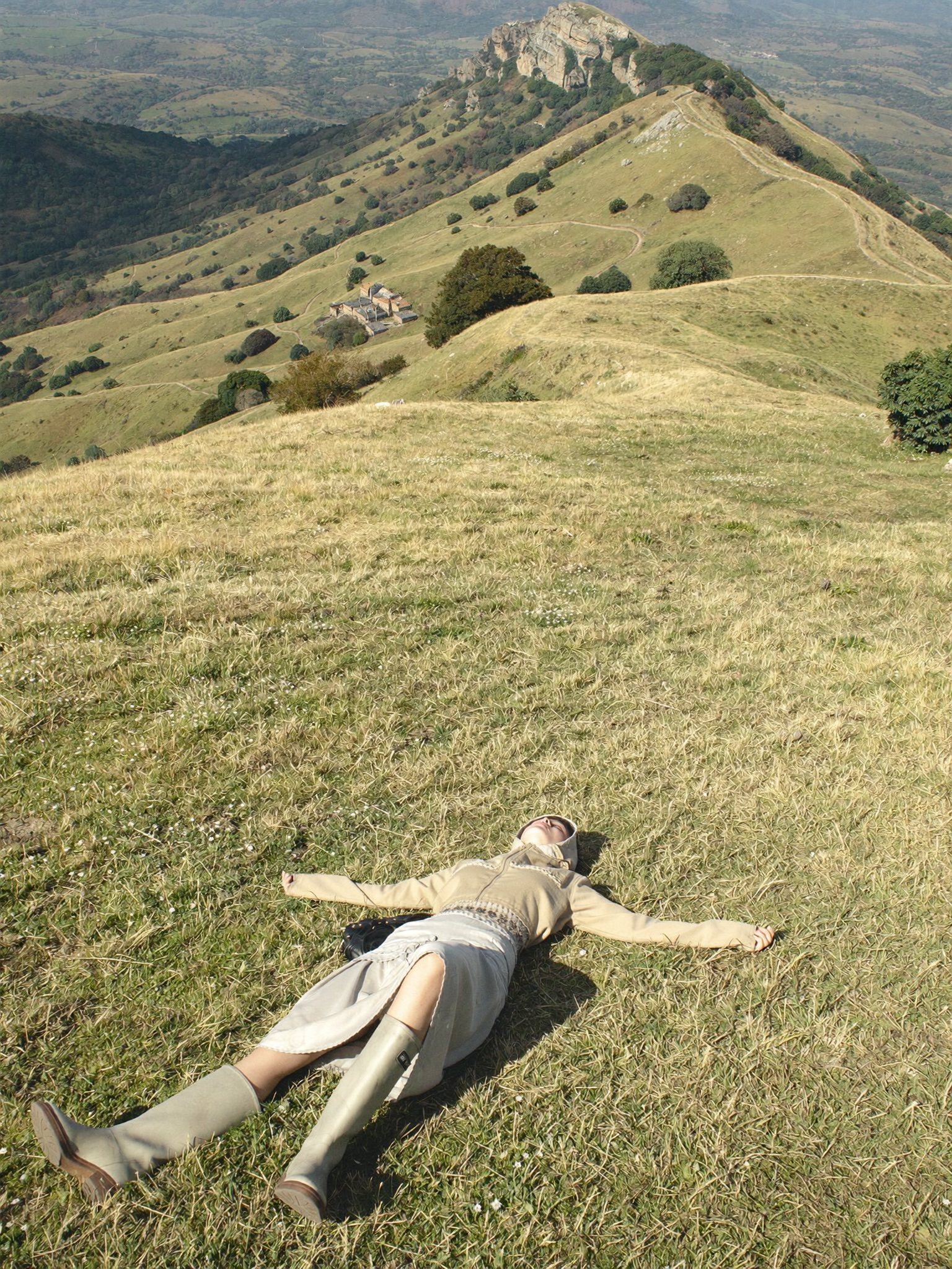 Person lying in tall grass on a hilltop overlooking rolling green hills