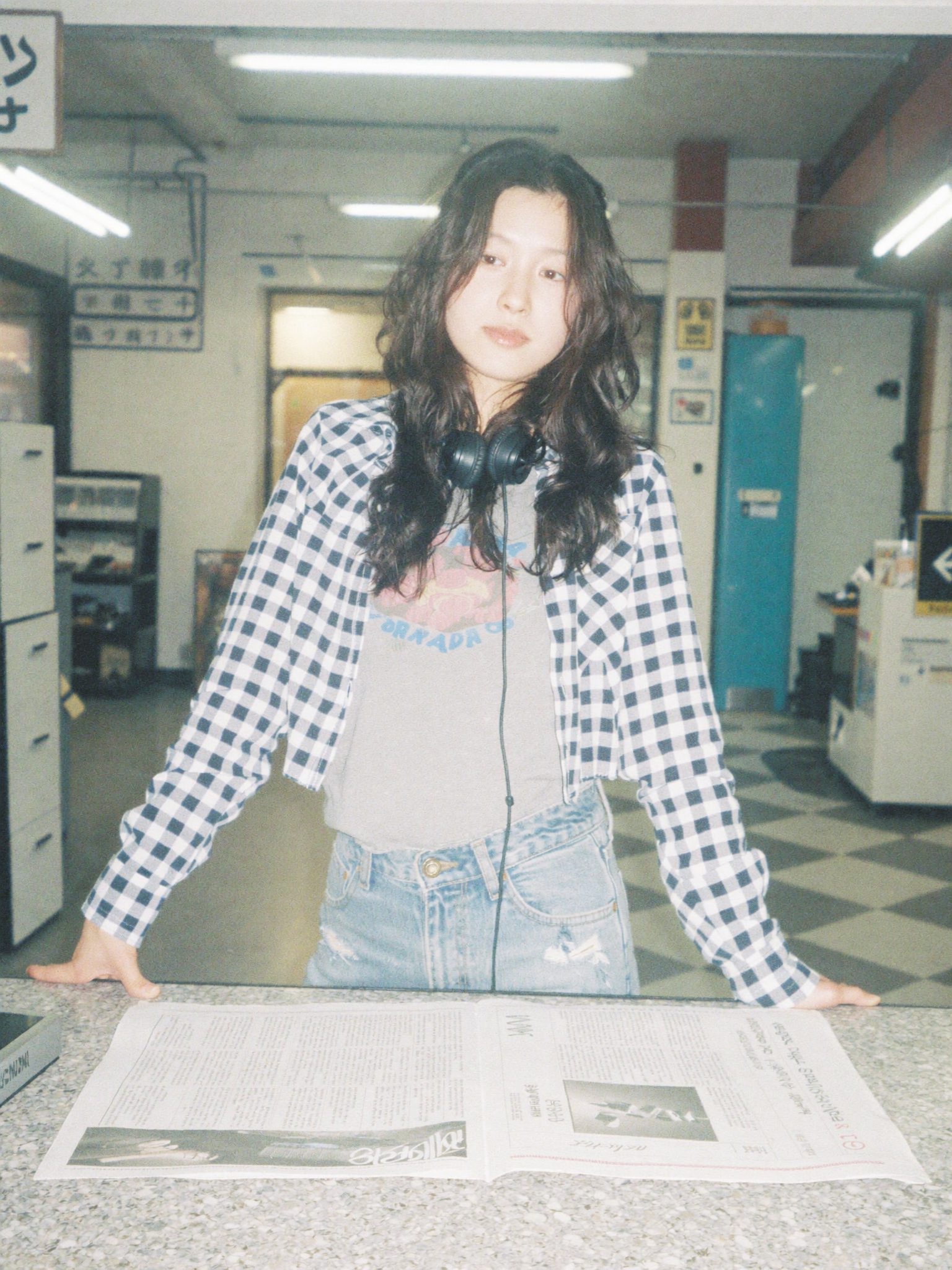 Woman with headphones around her neck reading a newspaper at a counter