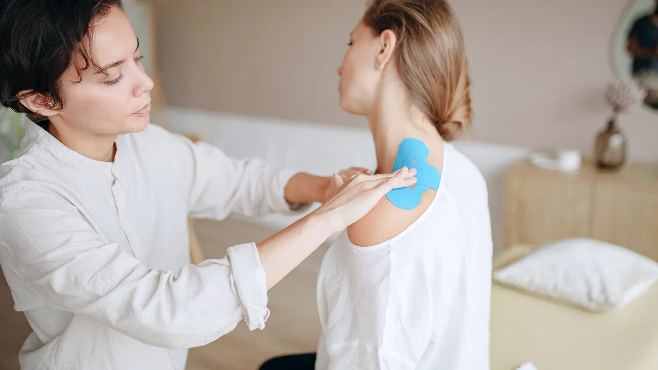 Physical therapist applying kinesiology tape to patient’s shoulder during wellness treatment.