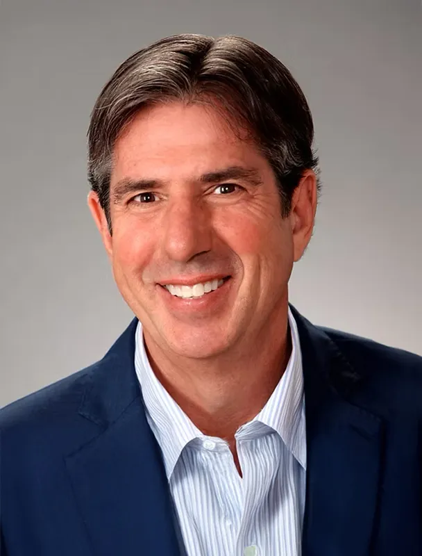 Professional headshot of smiling man in blue blazer and striped shirt.