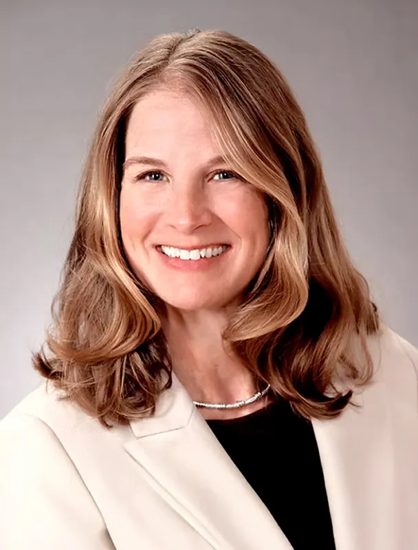 Professional headshot of smiling woman in light blazer and dark top.