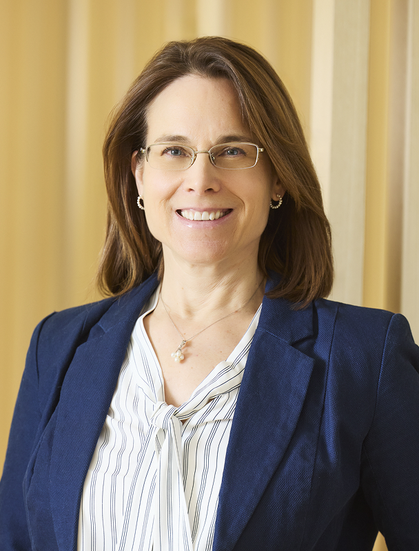Professional headshot of smiling woman wearing glasses and beige sweater.