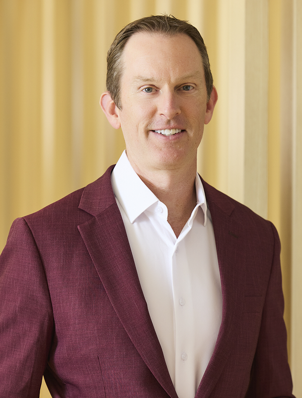Professional headshot of smiling man in light purple shirt and dark tie.
