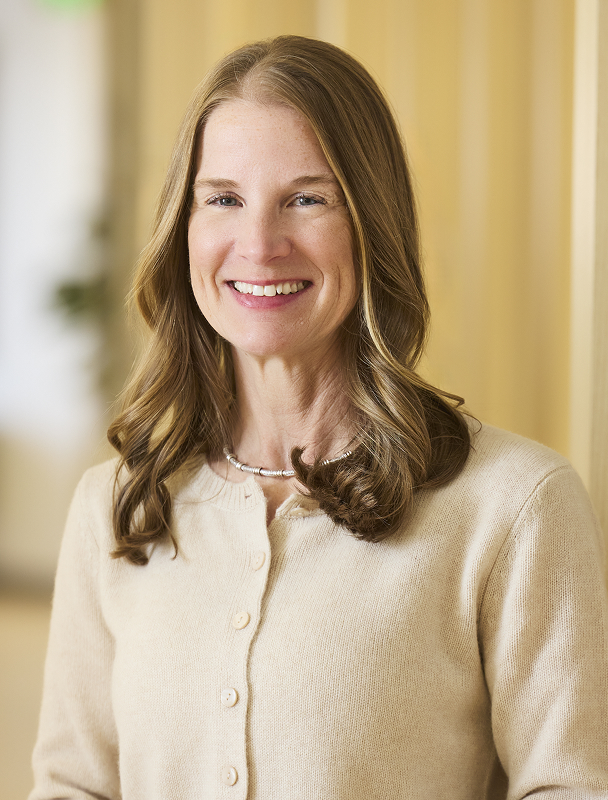 Professional headshot of smiling woman in light blazer and dark top.