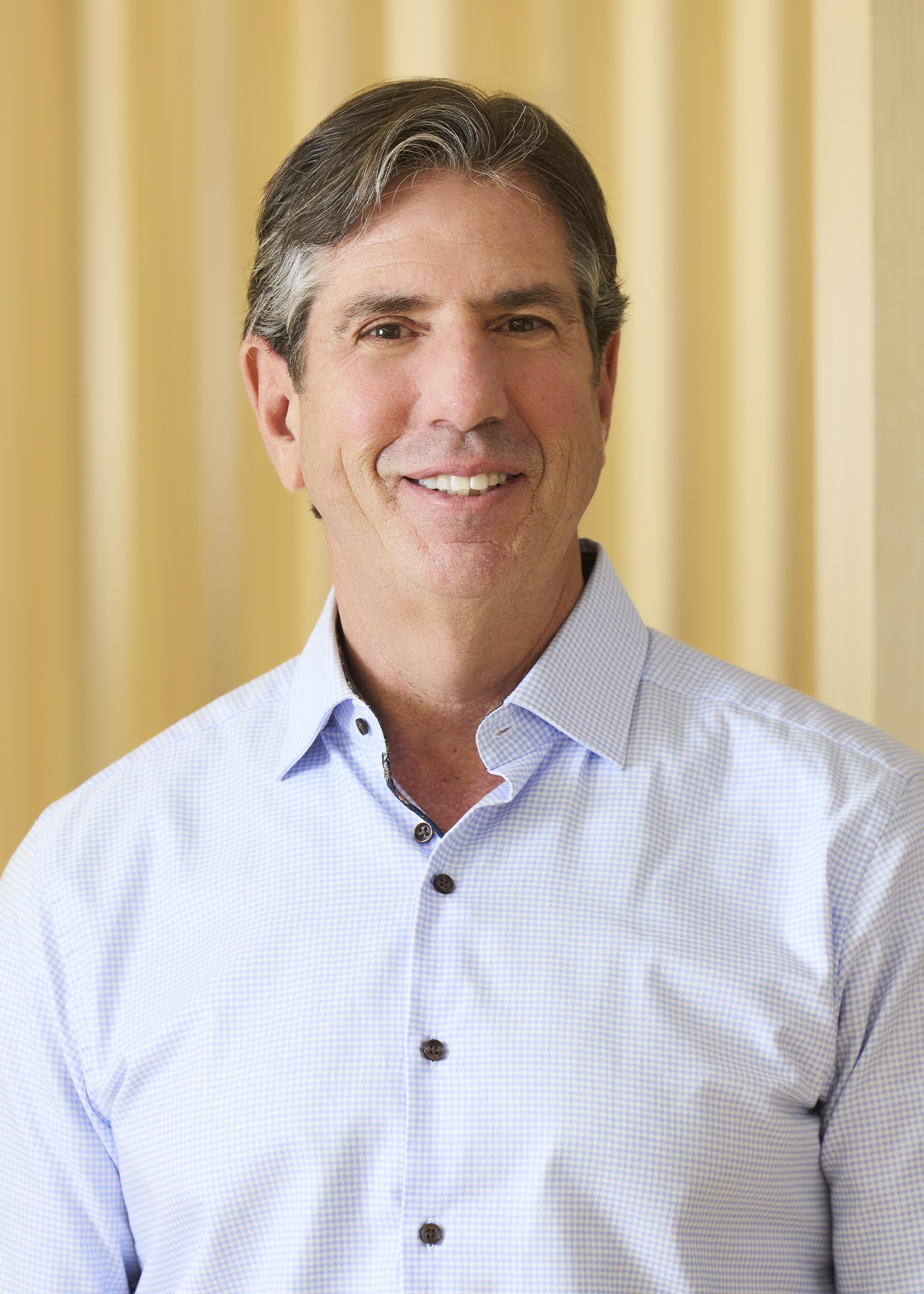 Professional headshot of smiling man in blue blazer and striped shirt.