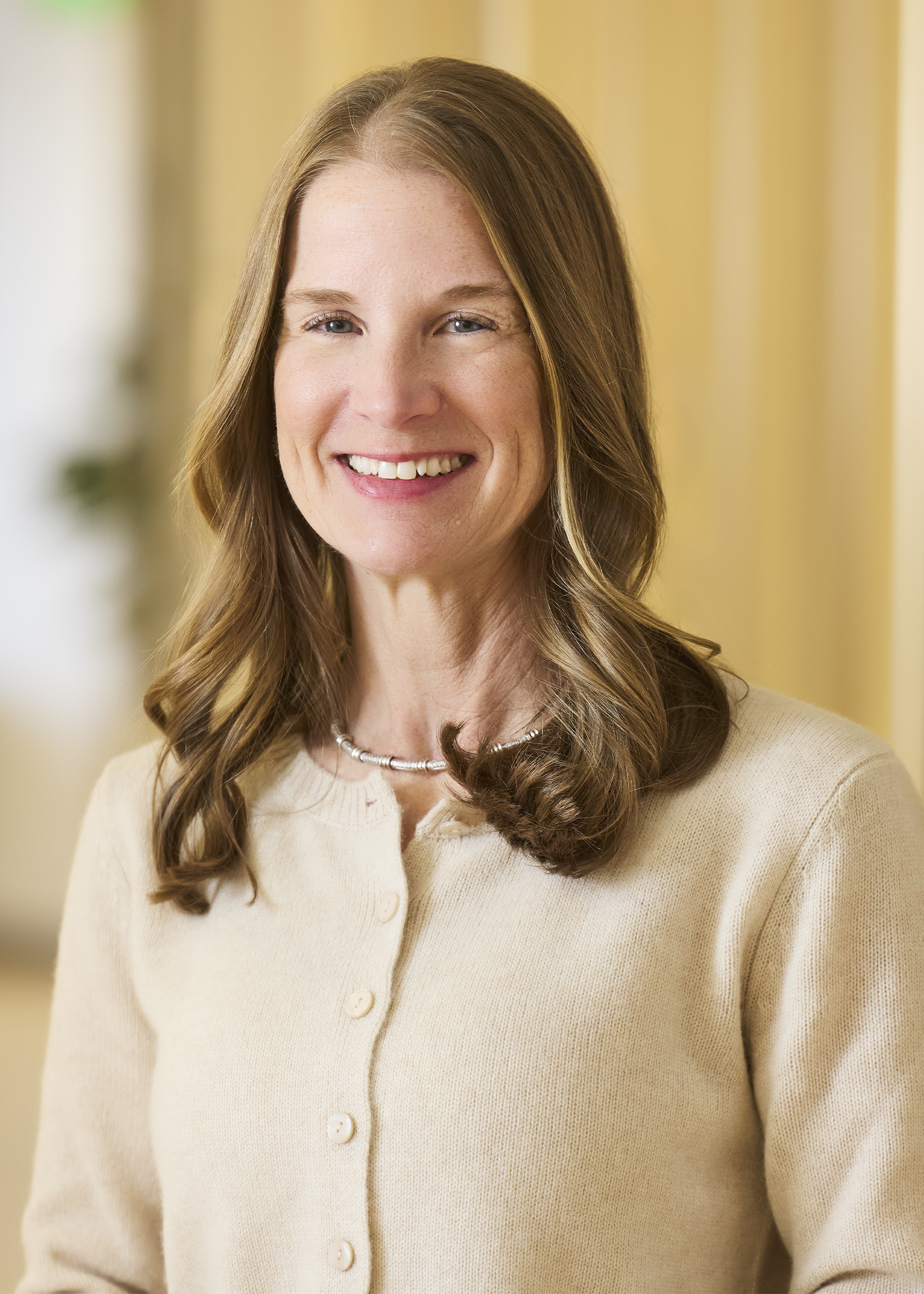 Professional headshot of smiling woman in light blazer and dark top.