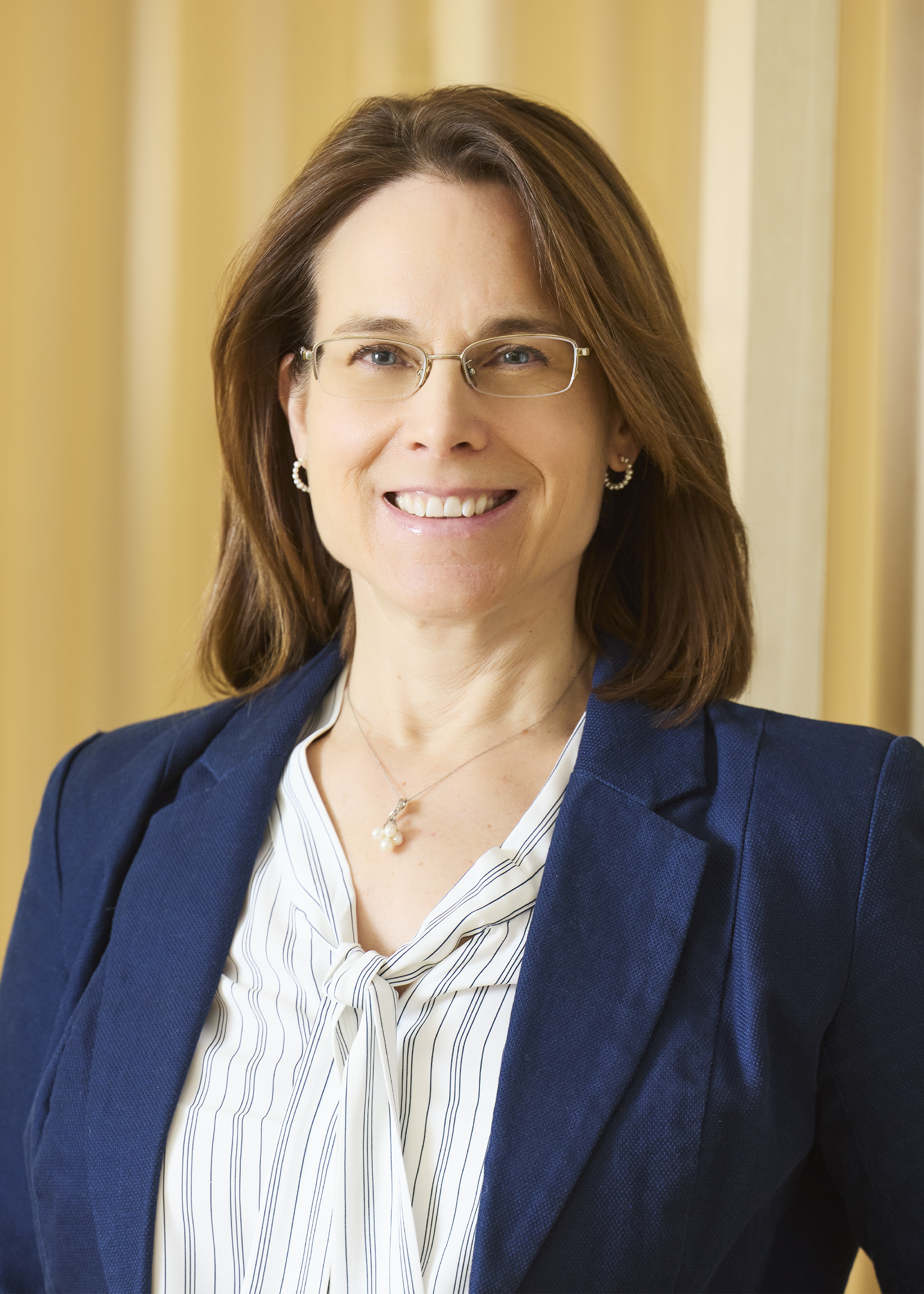 Professional headshot of smiling woman wearing glasses and beige sweater.