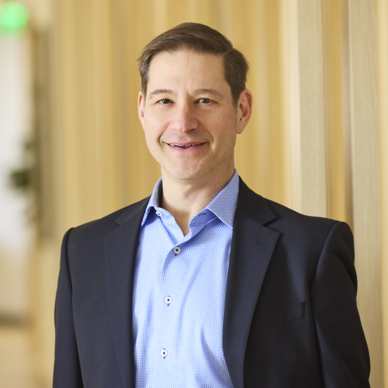 Professional headshot of smiling man in blazer and button-down shirt.