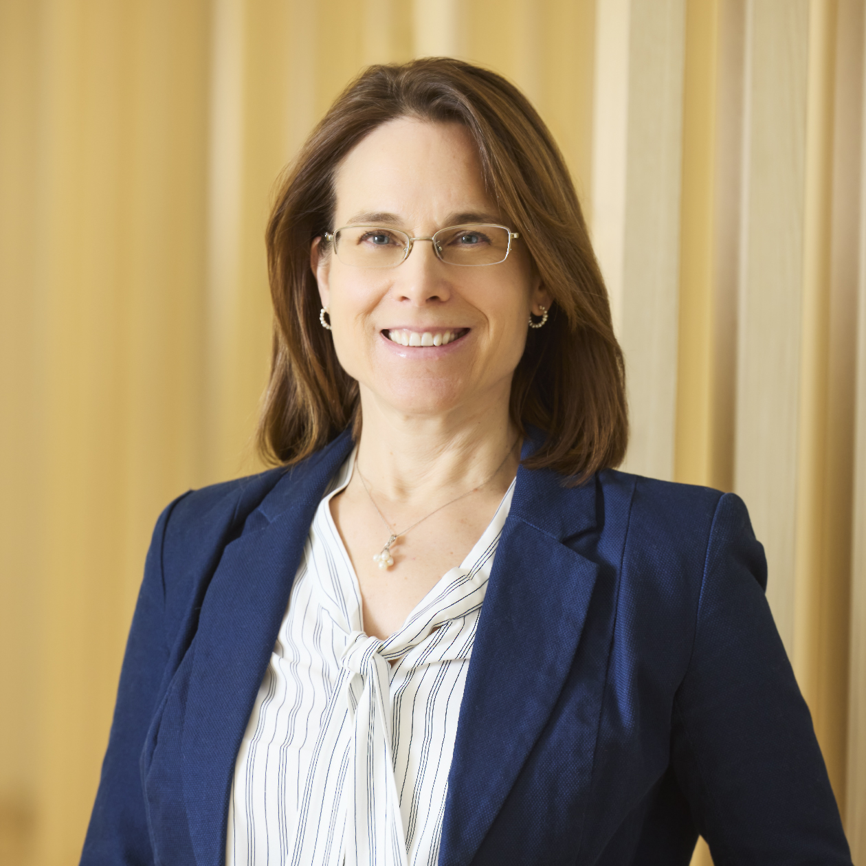 Professional headshot of smiling woman wearing glasses and beige sweater.