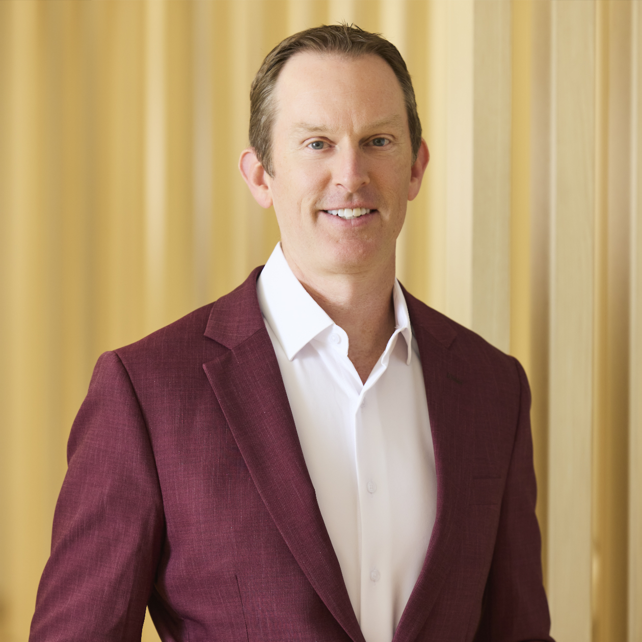 Professional headshot of smiling man in light purple shirt and dark tie.