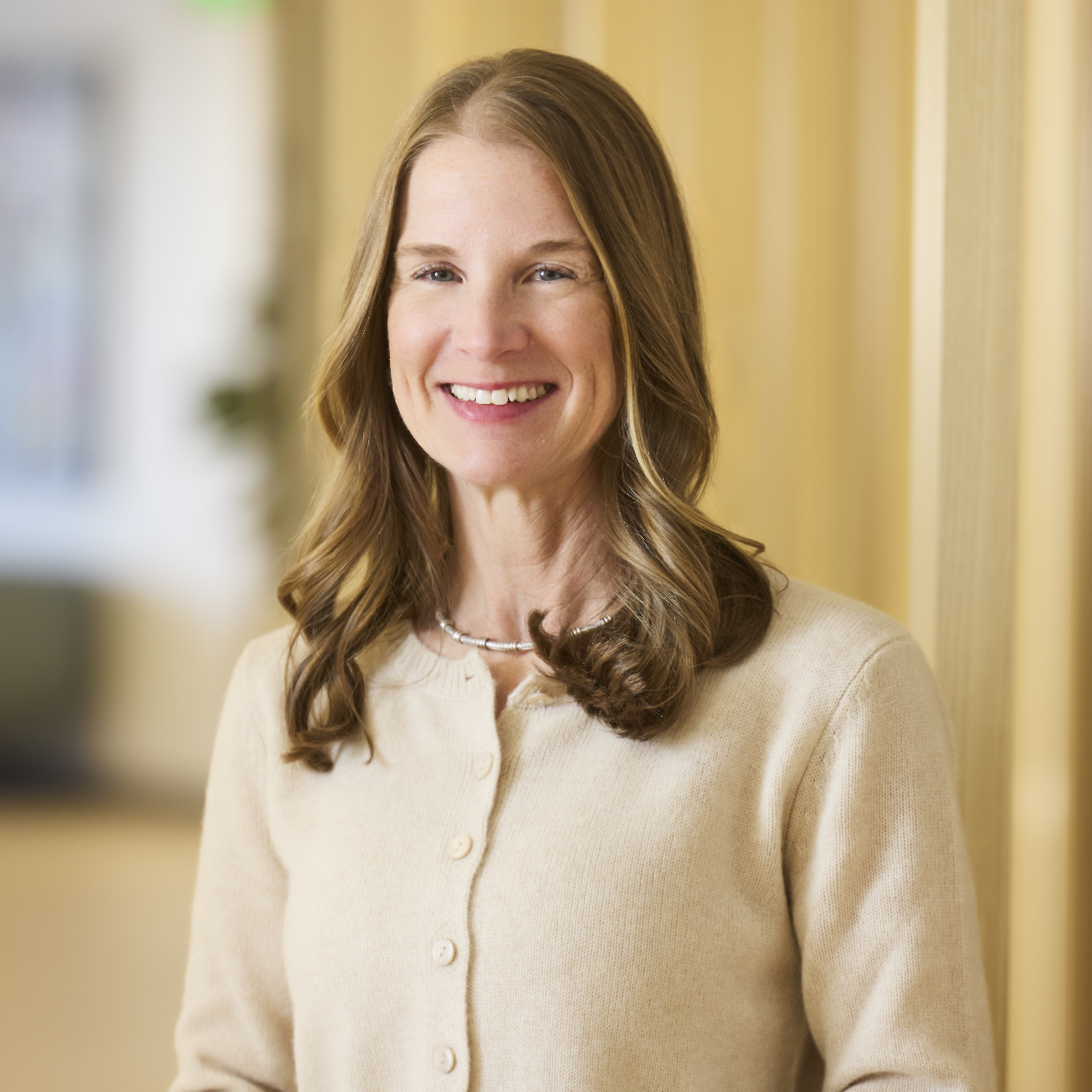 Professional headshot of smiling woman in light blazer and dark top.
