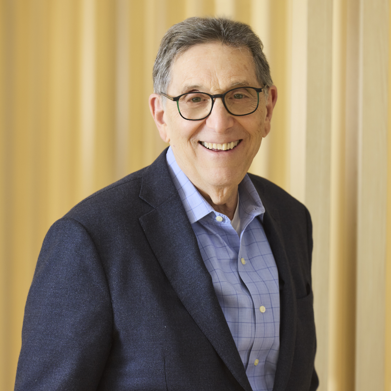 Professional headshot of smiling man wearing glasses, suit, and tie.