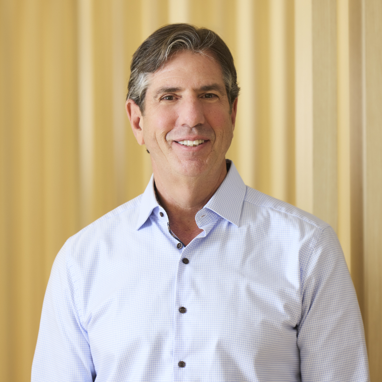 Professional headshot of smiling man in blue blazer and striped shirt.