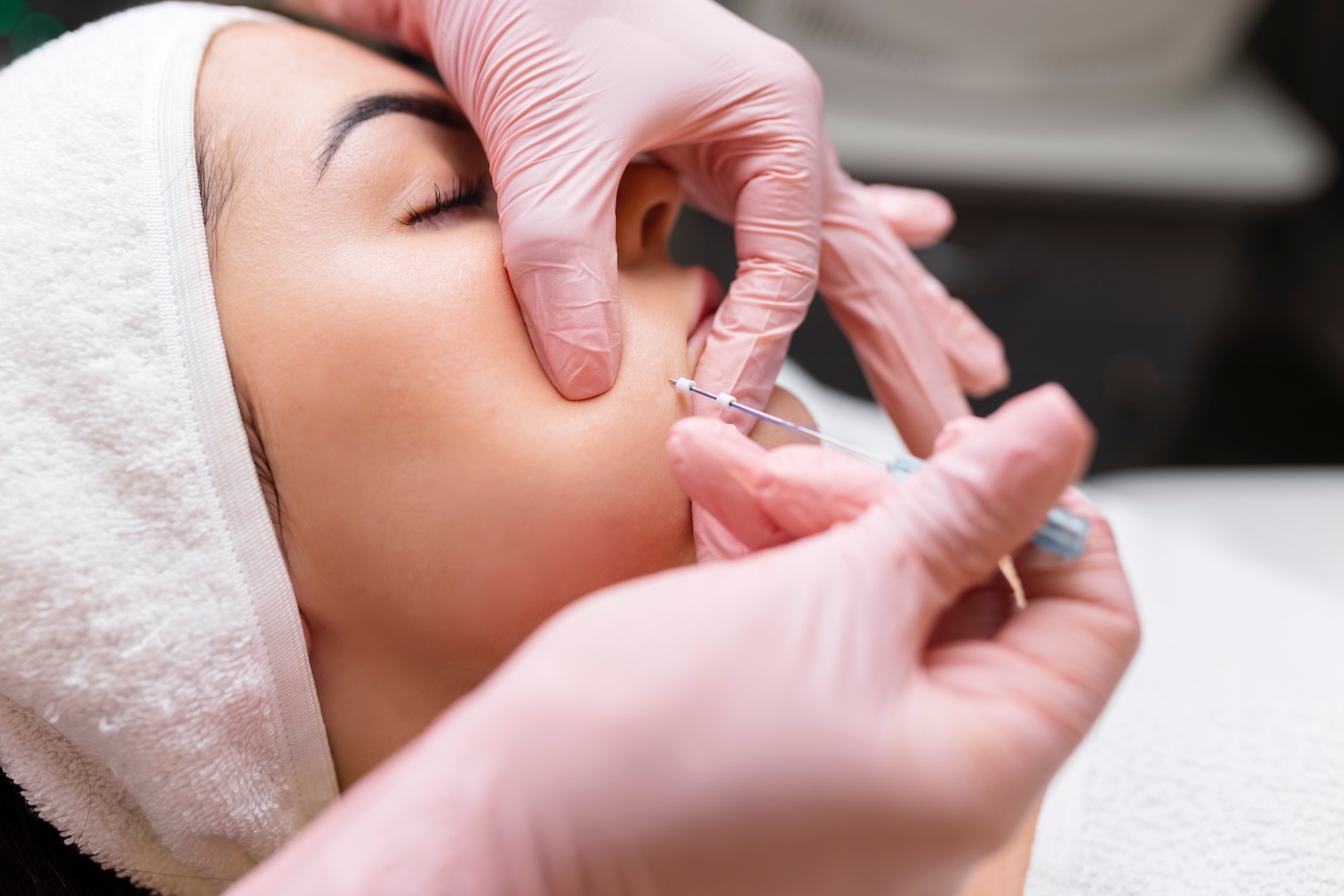 woman having facial procedure done by someone with pink gloves on