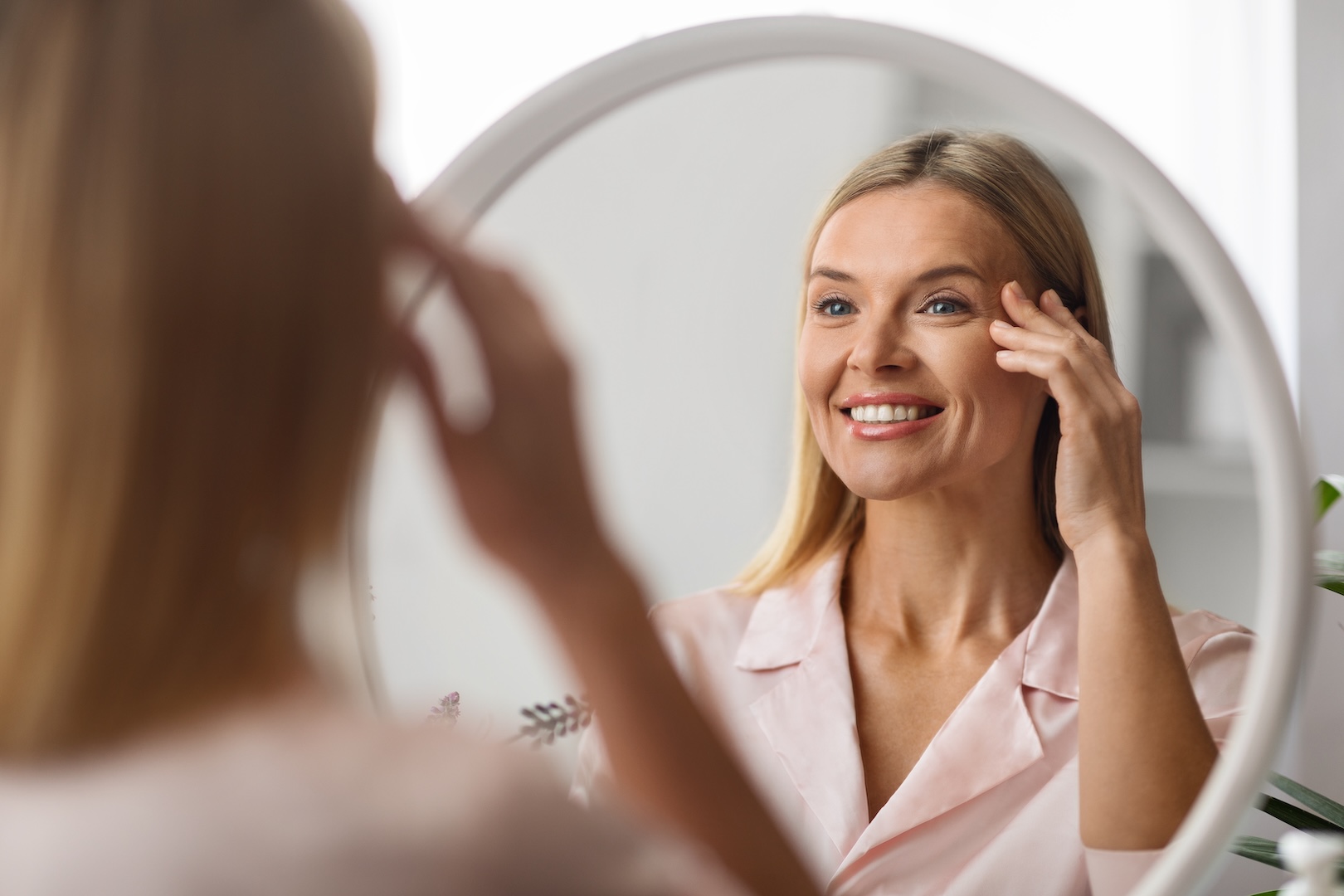 woman looking in mirror touching her face