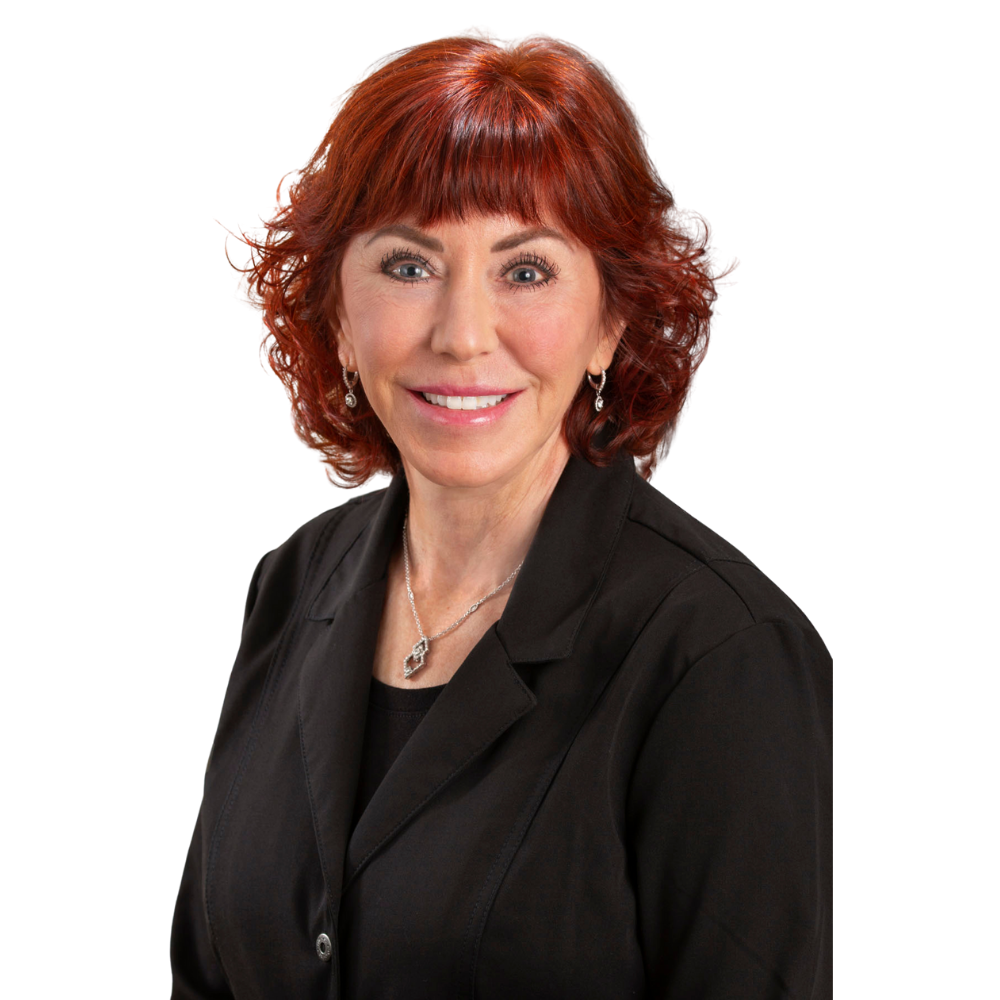 Smiling woman with curly red hair wearing a black blazer and silver jewelry against a white background.