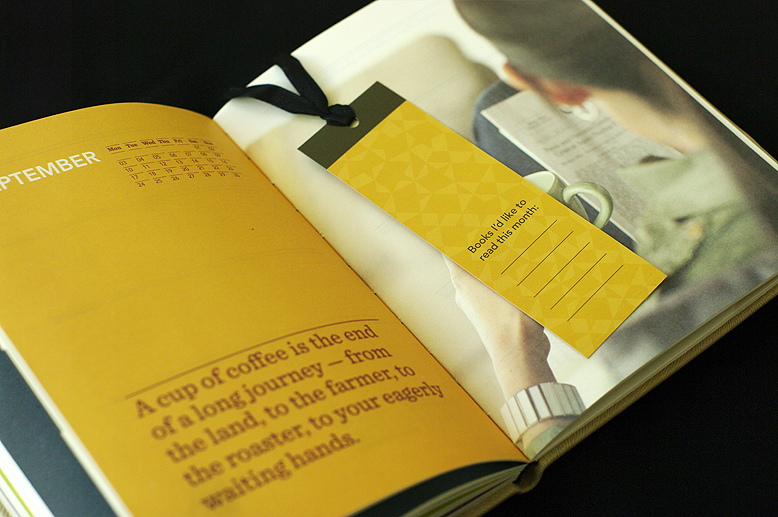 Interior spread from a Starbucks planner, showing a photograph of a person reading and drinking coffee. There is yellow printed bookmark with a chocolate brown ribbon inserted in the planner/