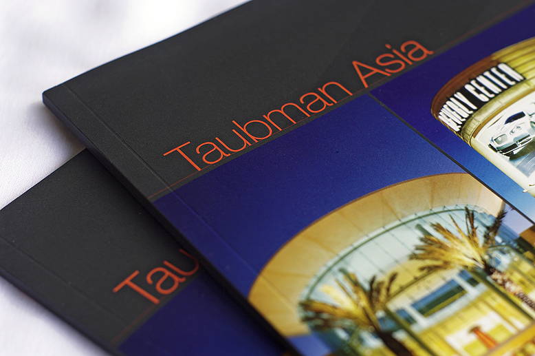 Close up photograph of the front of Taubman Asia annual report with a colorful photograph of a shopping mall and the name "Taubman Asia" in bright orange letters on a dark background