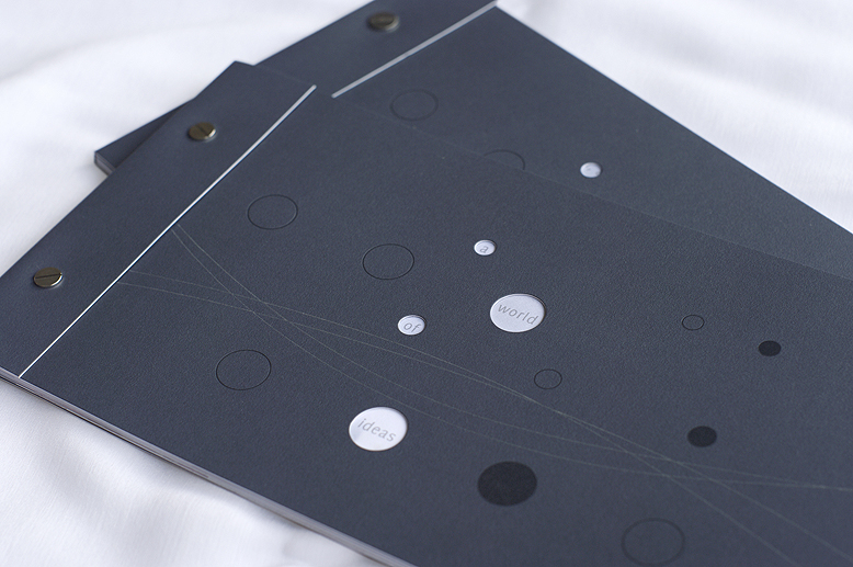 A slate gray brochure cover bound with screw posts and die cut with "bubble" holes. The words "A world of ideas" are visible through the 4 holes