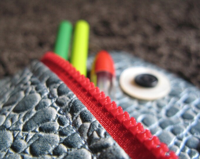Pouch in the shape of a monster with large button eyes and a red zipper.