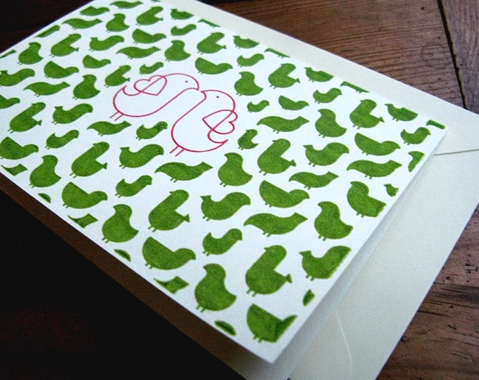 Riso print in green and pink ink, with a pair of pink birds against a backdrop of green birds
