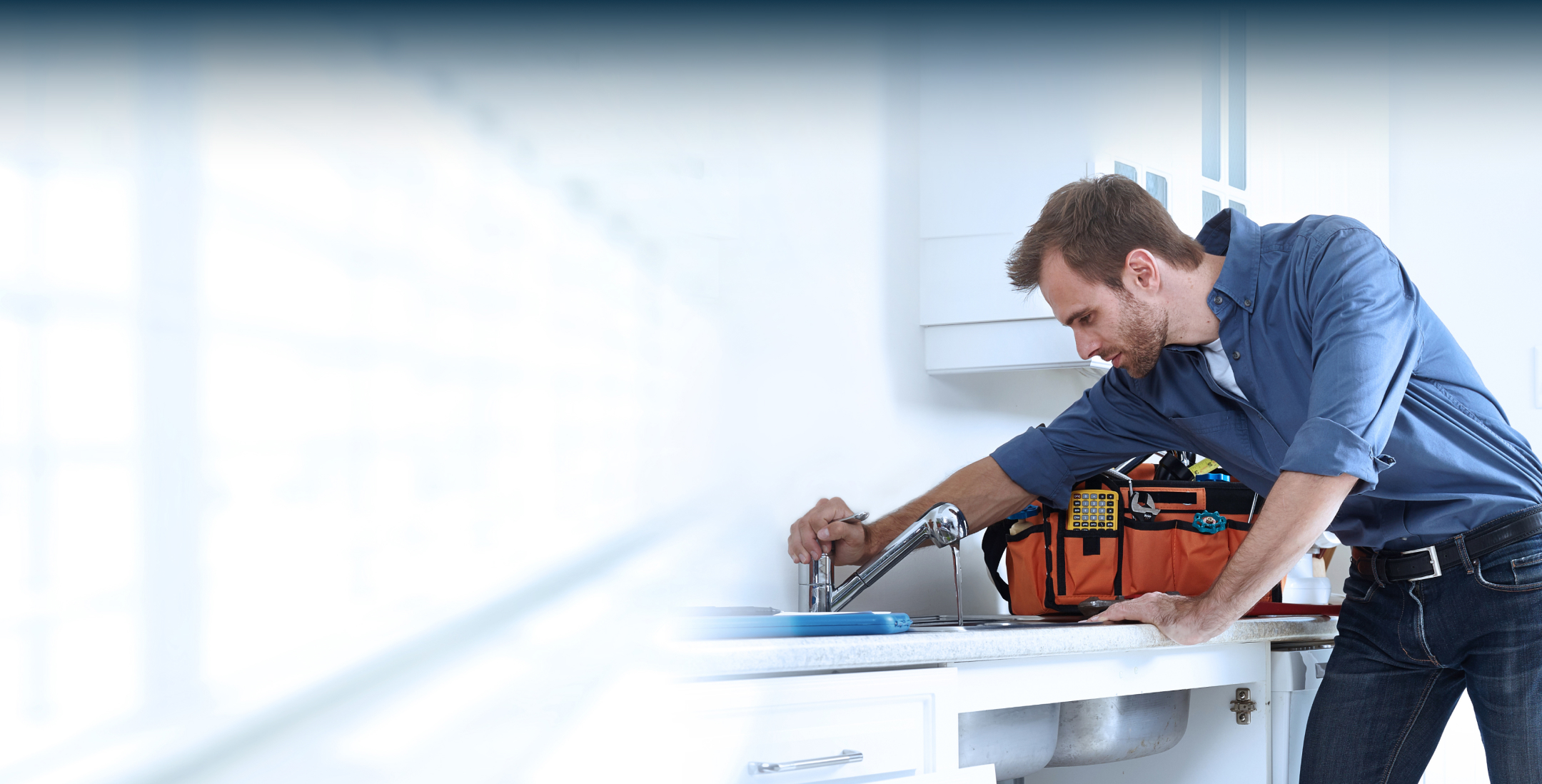 Man in blue shirt fixing a kitchen sink faucet with an open toolbox on the counter.