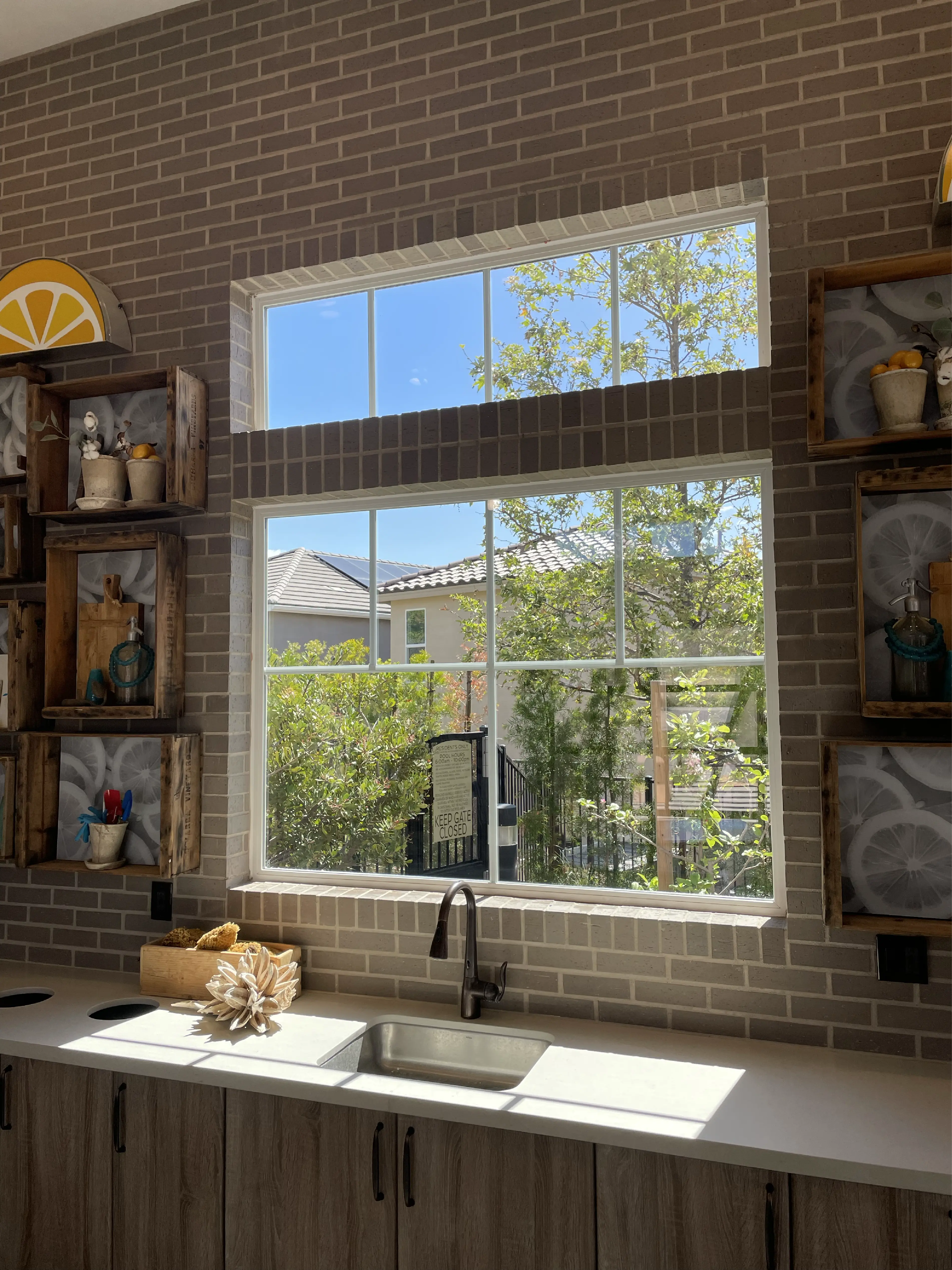Kitchen countertop with wooden cabinets, stainless steel sink under a large window showing greenery and rooftops outside.