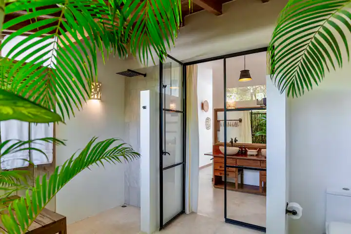 Modern bathroom with glass door shower, wooden countertop with twin sinks, green plants framing the scene.