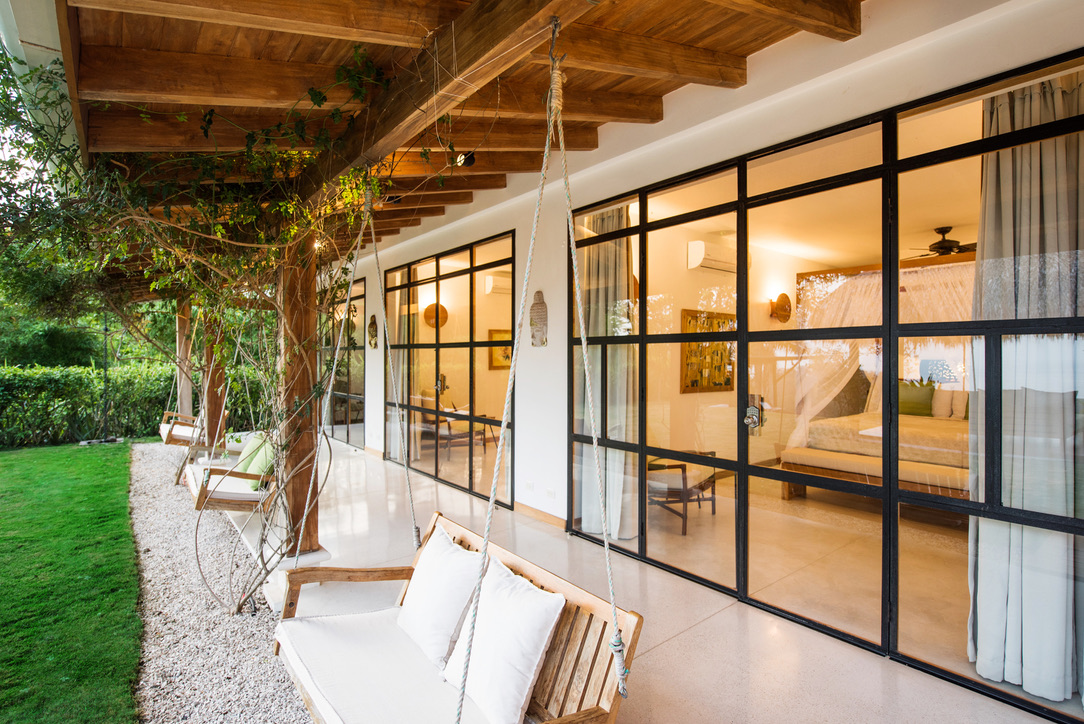 Wooden porch with hanging swing chairs and large glass sliding doors revealing a bedroom inside.