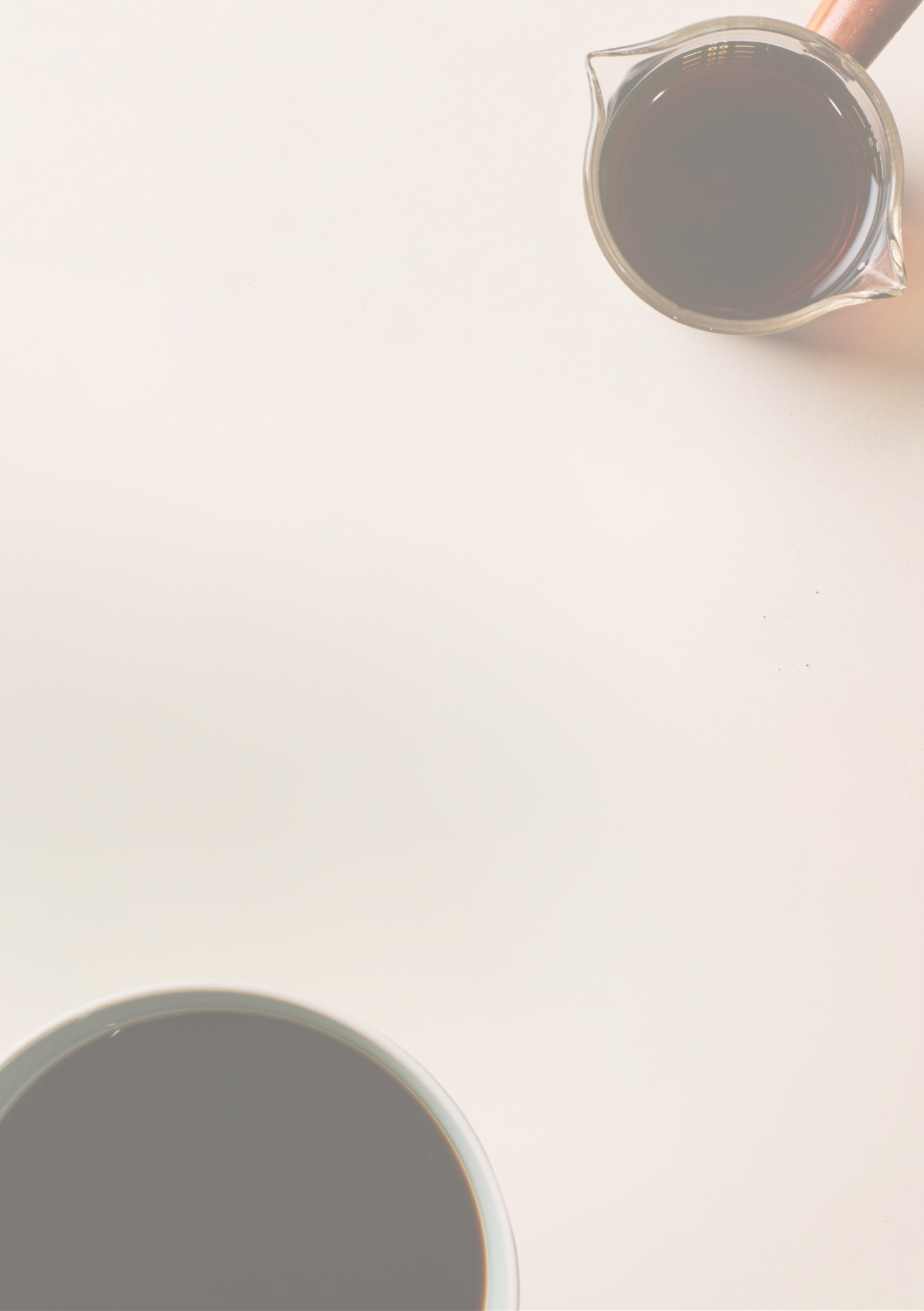 Overhead view of a cup and a glass pitcher filled with black coffee on a pale surface.