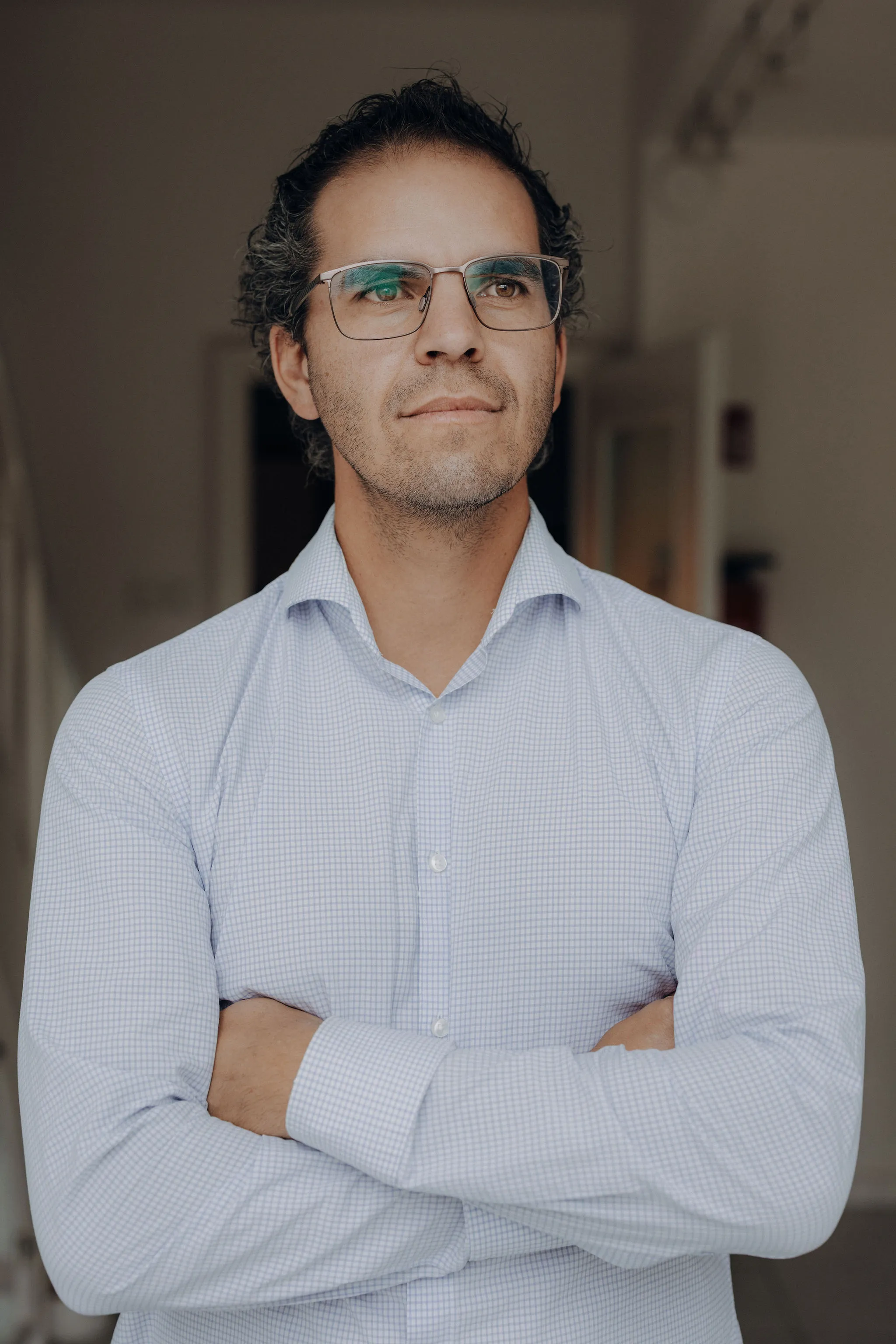 Mann mit Brille und hellblauem Hemd schaut selbstbewusst mit verschränkten Armen nach rechts.