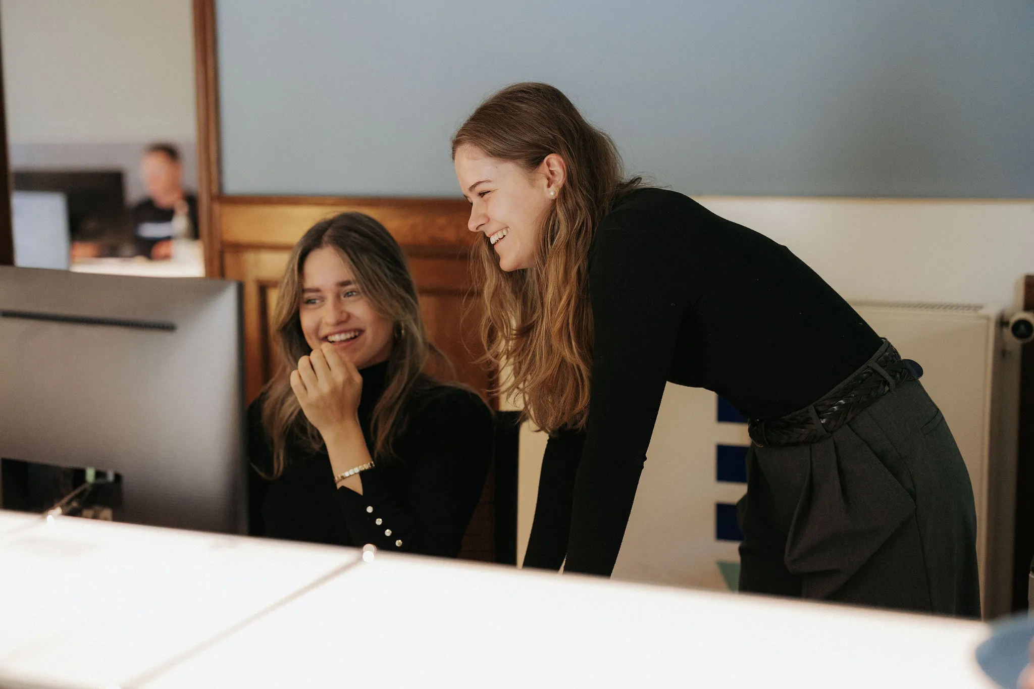 Zwei Frauen lachen und schauen zusammen auf einen Computerbildschirm im Büro.